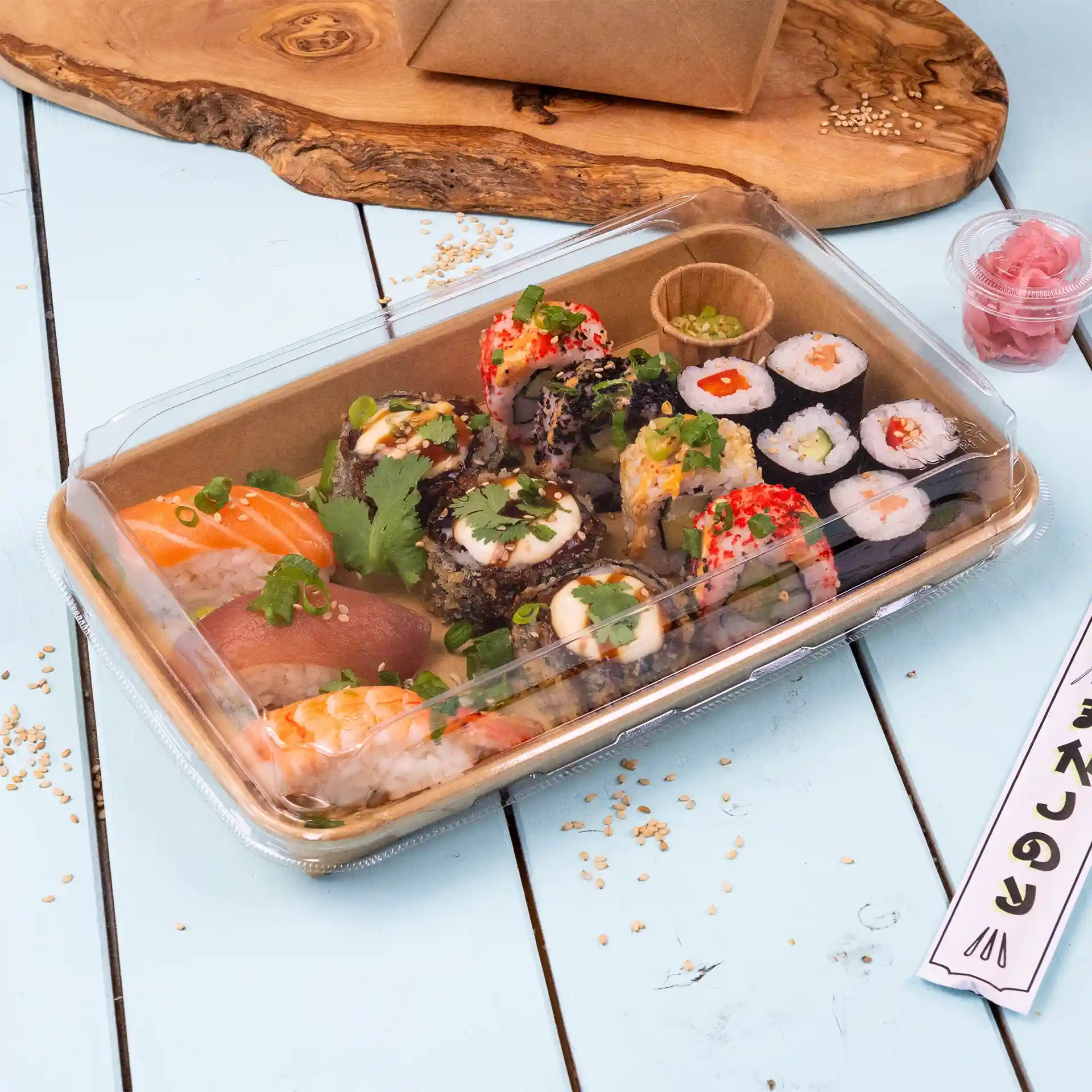 Transparante sushi-doosdeksel met verschillende sushirollen, waaronder zalm en tonijn, gegarneerd met kruiden en geserveerd met ingelegde gember.