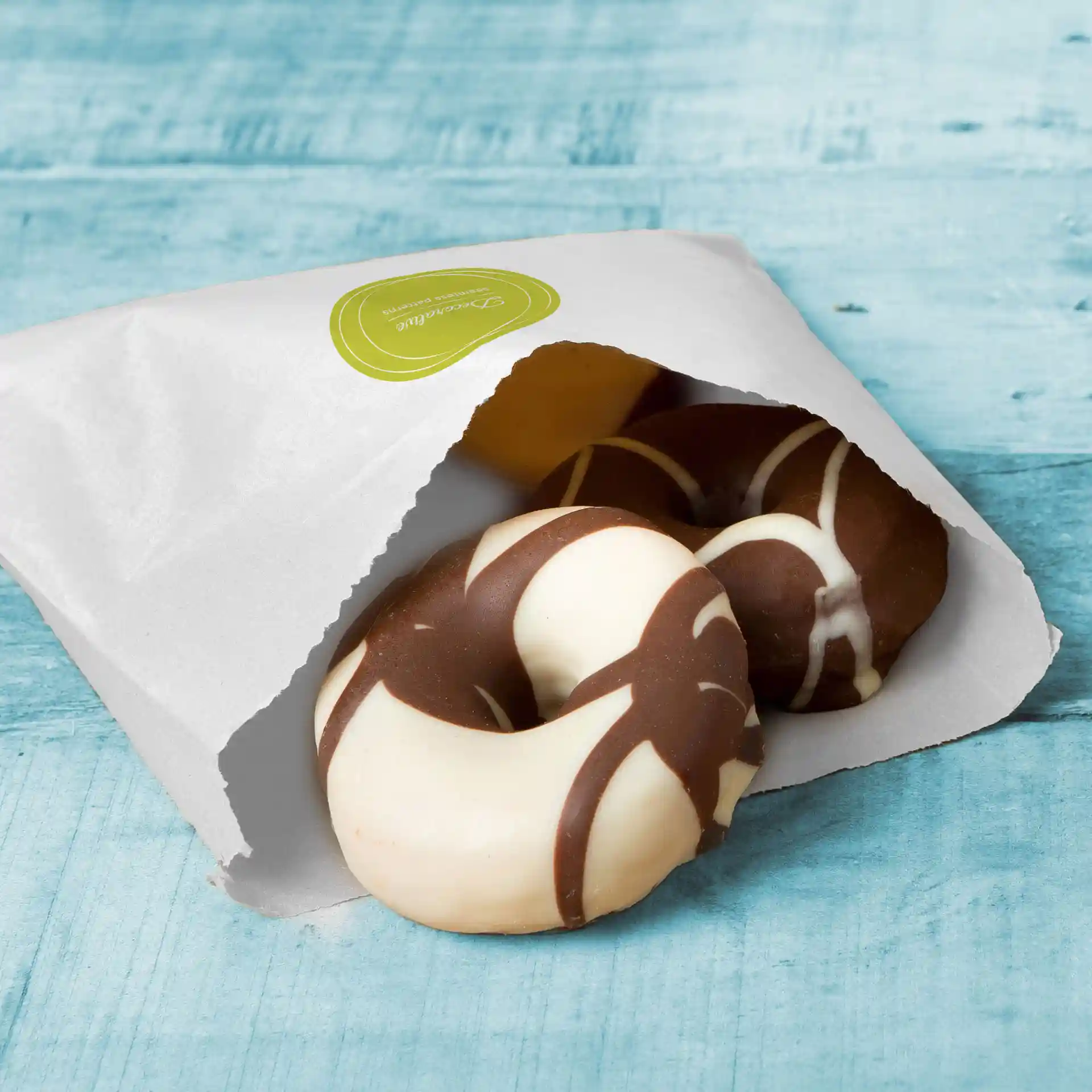 Witte platte tas gedeeltelijk open, met twee ronde koekjes met chocolade- en witte glazuurontwerpen.