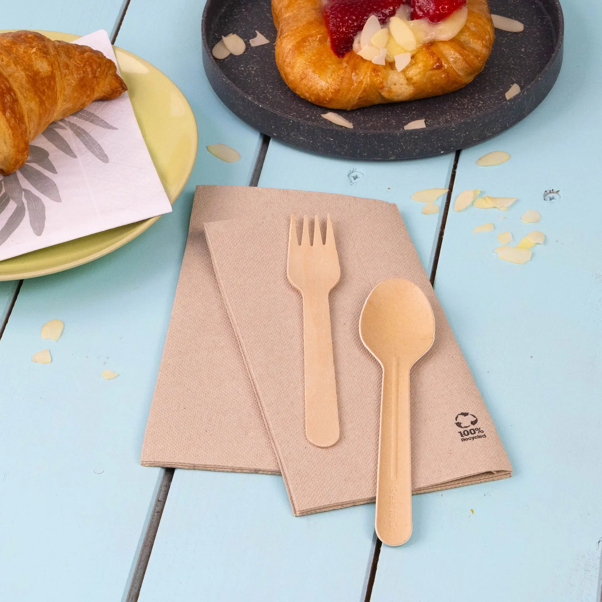 Gerecycled papier servetten met een vork en lepel op bruine servetten, tegen een blauwe houten tafel.