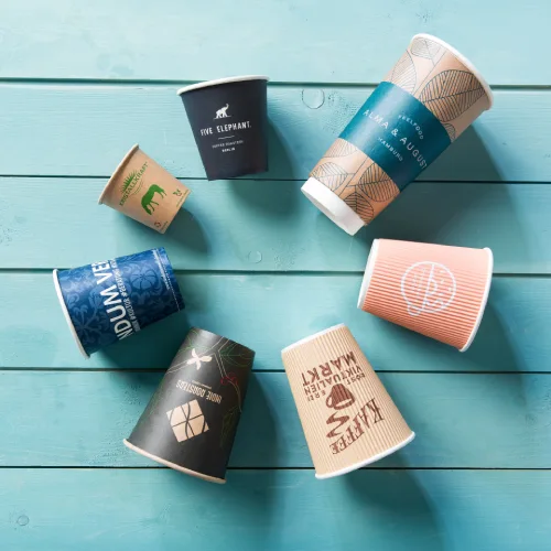Diverse wegwerpbekers met unieke ontwerpen verspreid over een turquoise houten oppervlak.