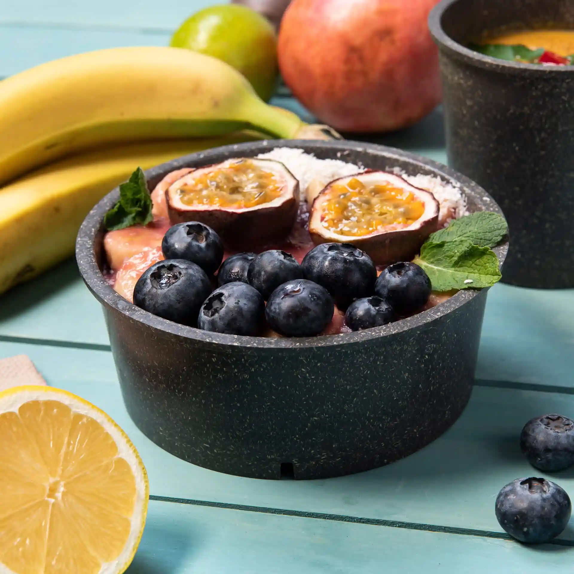 Ronde grijze herbruikbare kom gevuld met fruit, waaronder bosbessen en passievrucht, op een houten oppervlak.