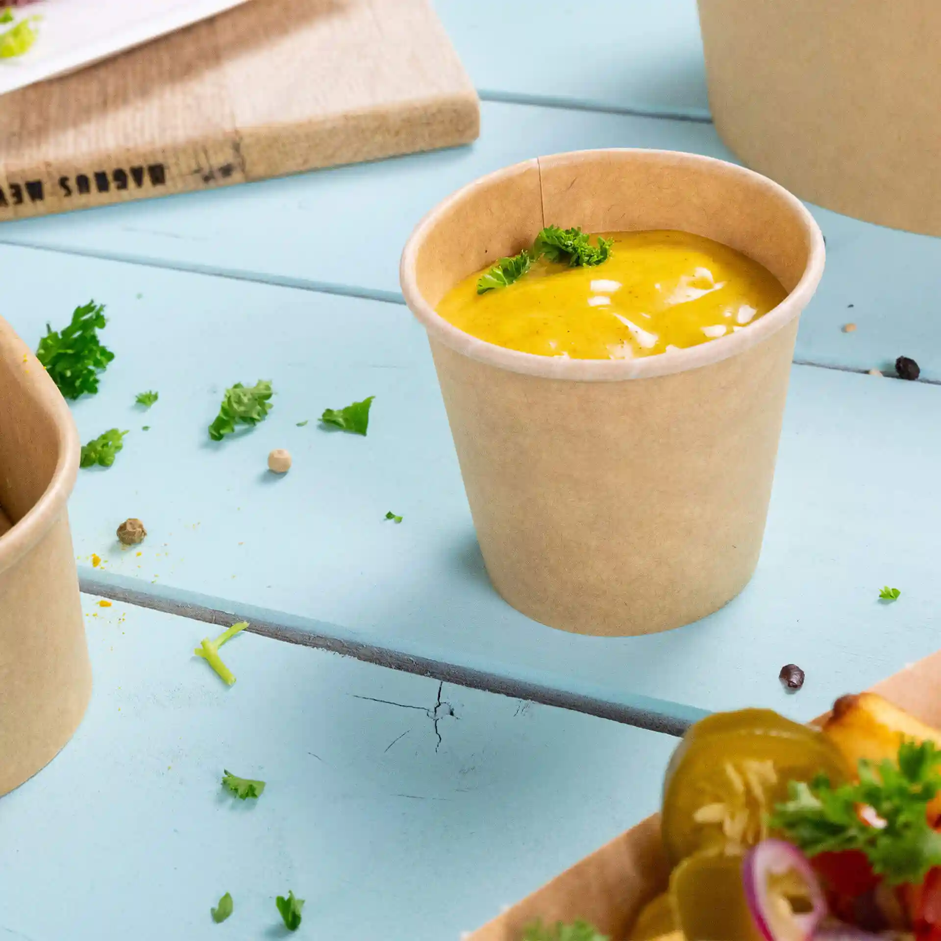 Bruine ronde deli-container met een gecoate binnenkant, gevuld met gele saus en getopt met een klein stukje peterselie.