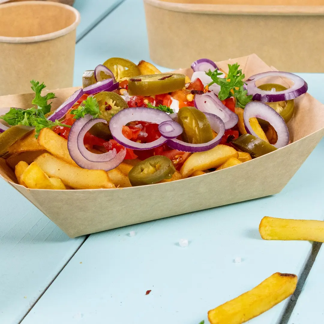 Kom met frietjes, belegd met gesneden uien, jalapeños, blokjes tomaat en peterselie op een blauwe ondergrond.