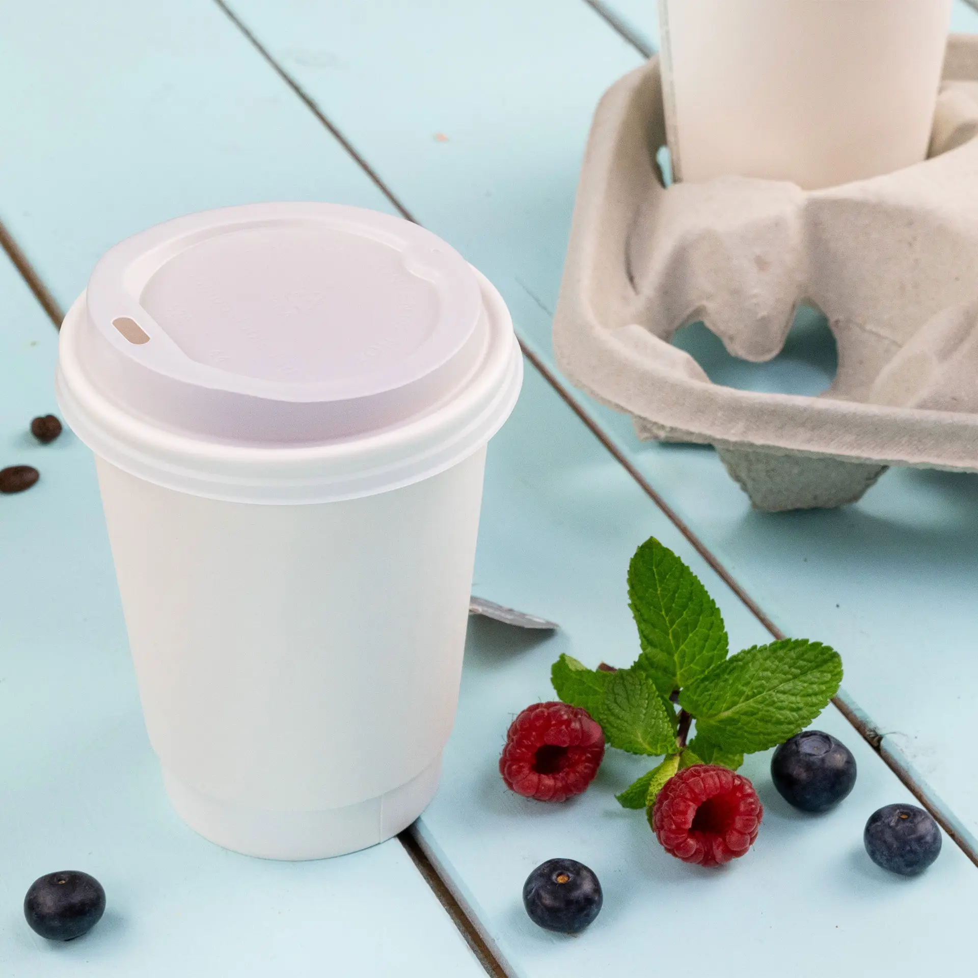 Een witte dubbelwandige koffiebeker om mee te nemen met een PLA binnencoating, vergezeld van frambozen, blauwe bessen en muntblaadjes.