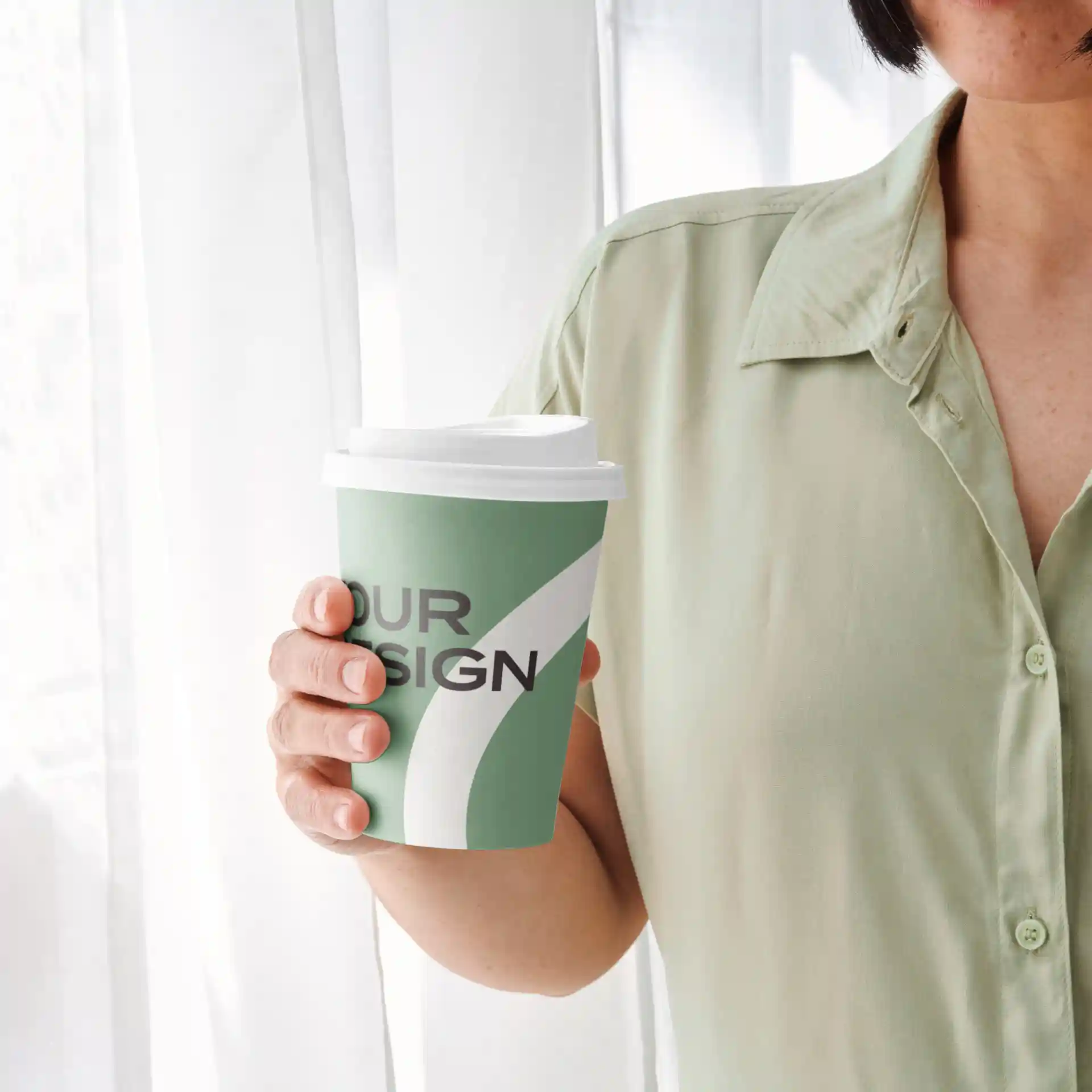 Groene papieren beker met een witte deksel, met een ontwerp en vastgehouden door een persoon in een lichtgroen shirt.