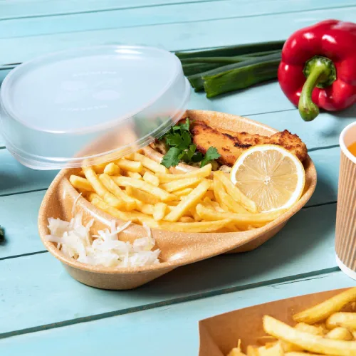 Voedselcontainer met gebakken vis, citroen, frietjes en salade, vergezeld van lente-uitjes en een rode paprika.