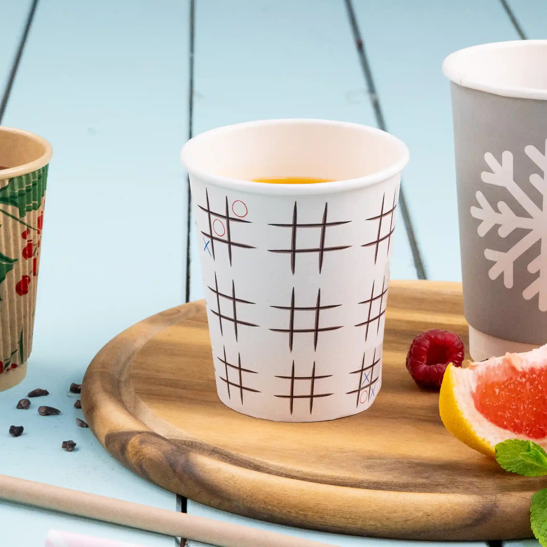 Witte beker met een tic-tac-toe patroon, geplaatst op een houten dienblad met fruit en een andere beker in de buurt.