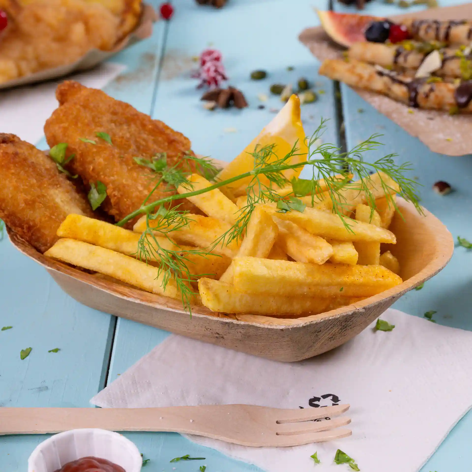 Diepe palmbladboot gevuld met frietjes, twee gefrituurde visstukken, een partje citroen en een takje dille.
