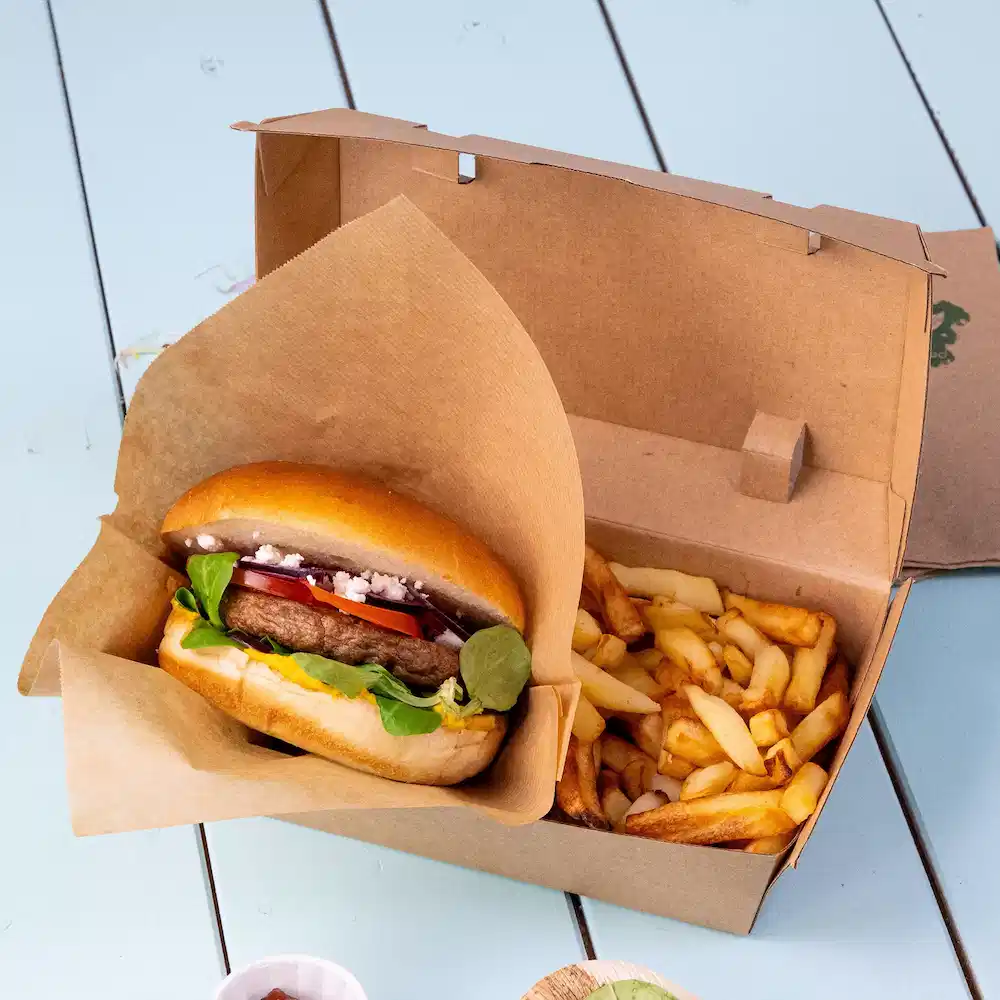 Burger met toppings in een afhaaldoos naast een portie friet.