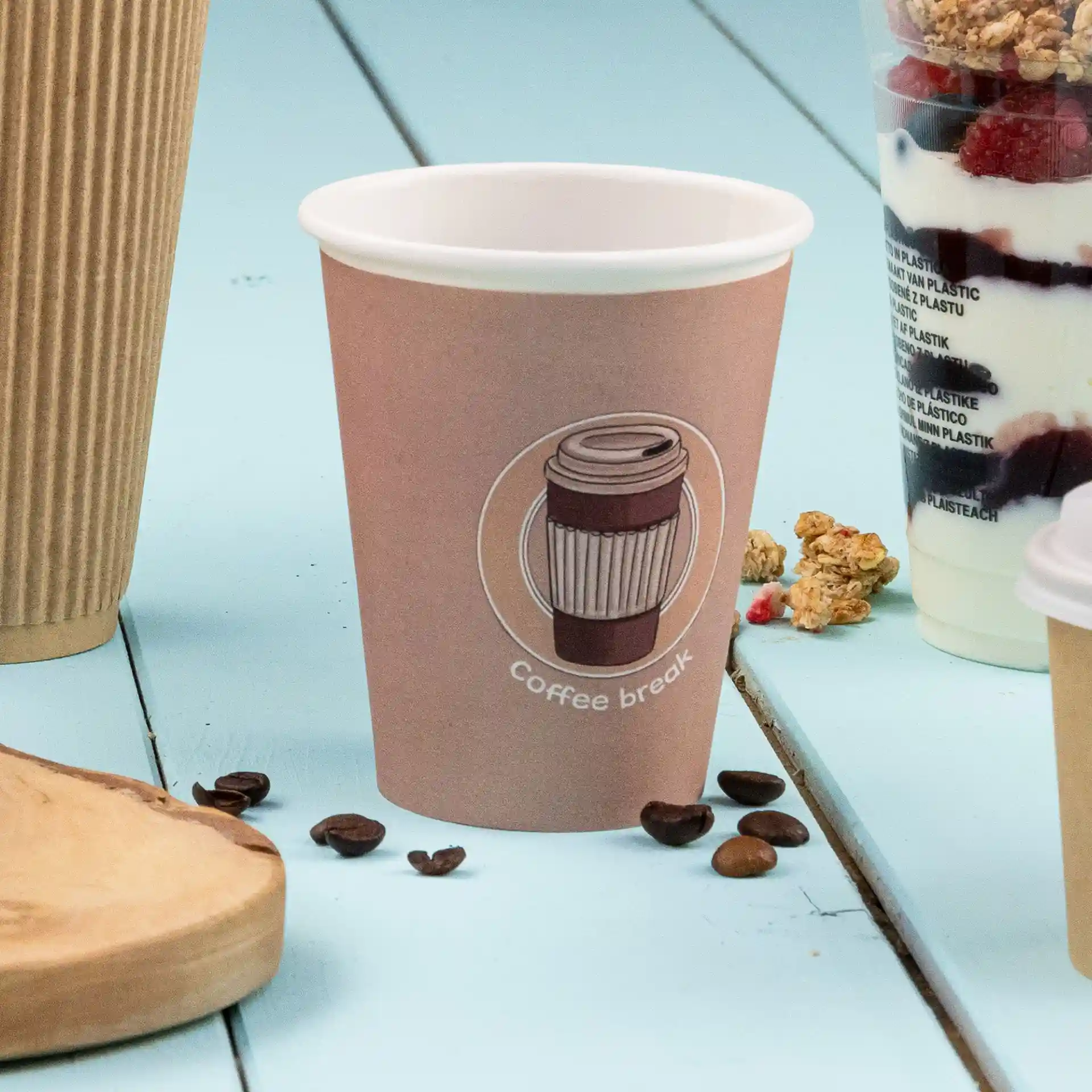 Bruine papieren beker met een gedrukt koffiedesign en tekst, geplaatst op een blauwe ondergrond met koffiebonen in de buurt.
