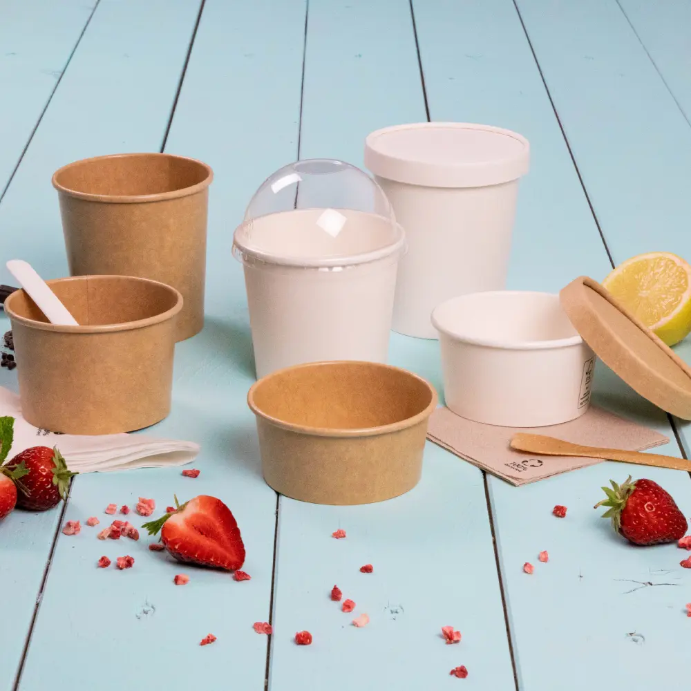 Dessertcontainers voor afhaalmaaltijden in verschillende maten, van papier en plastic, omringd door aardbeien en citroen.
