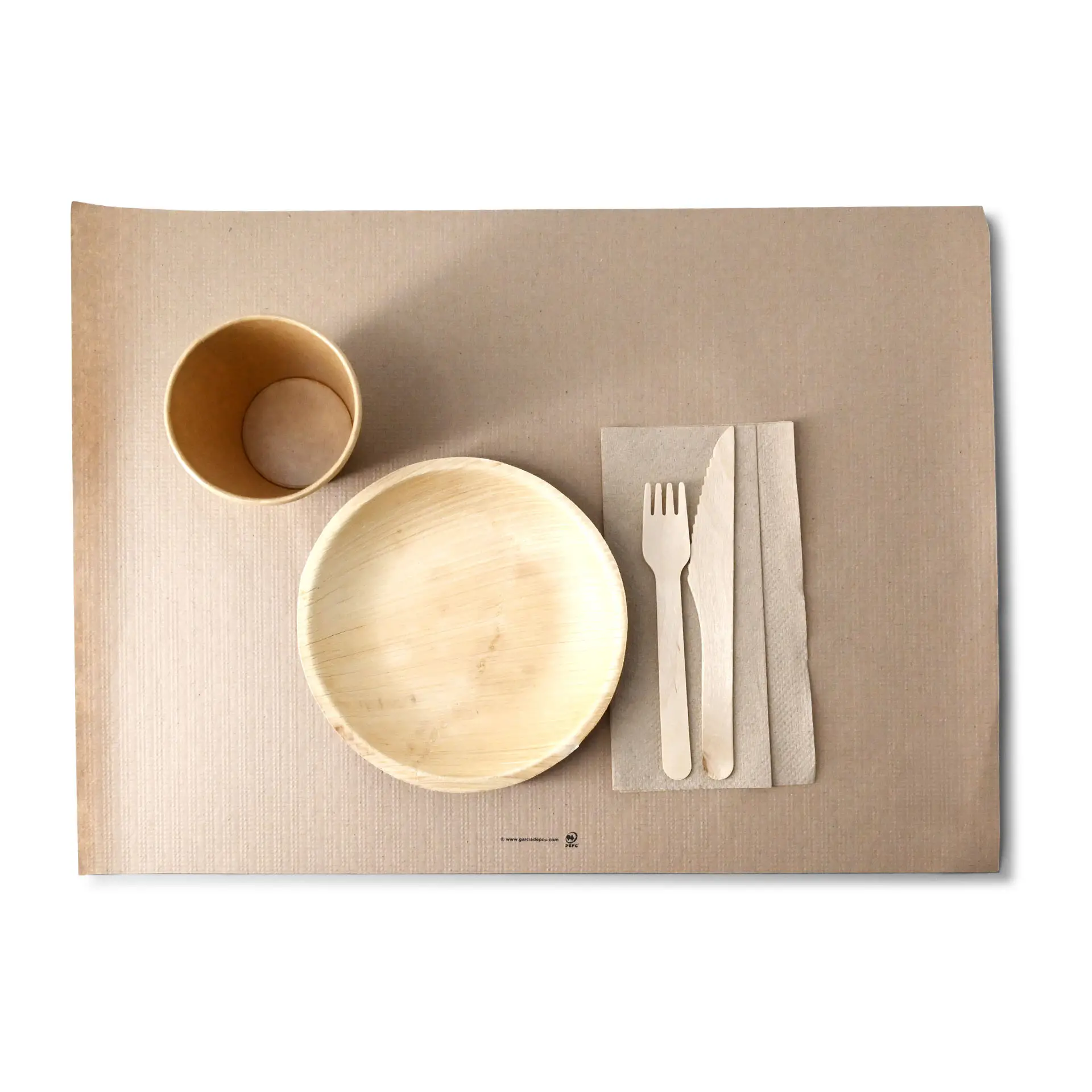 Afbeelding van een papieren placemat met een kom, beker, houten vork, mes en servet erop.