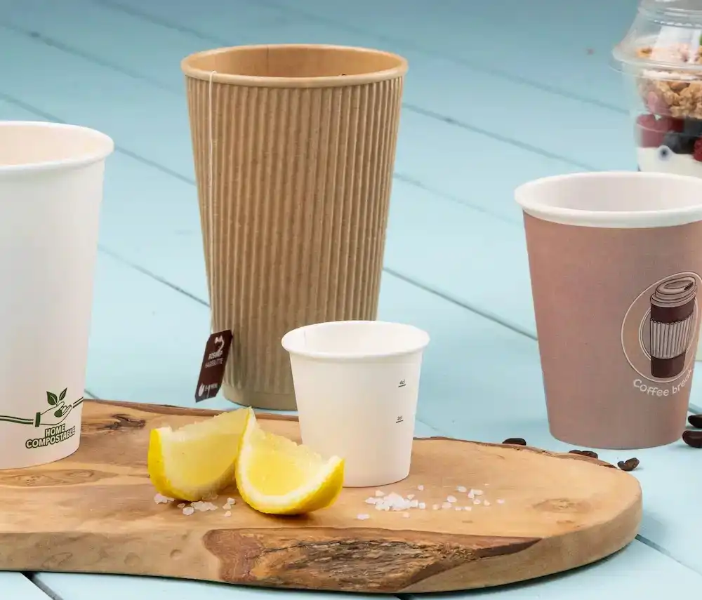 Assortiment papieren bekers op een houten oppervlak met citroenpartjes en zoutkristallen.