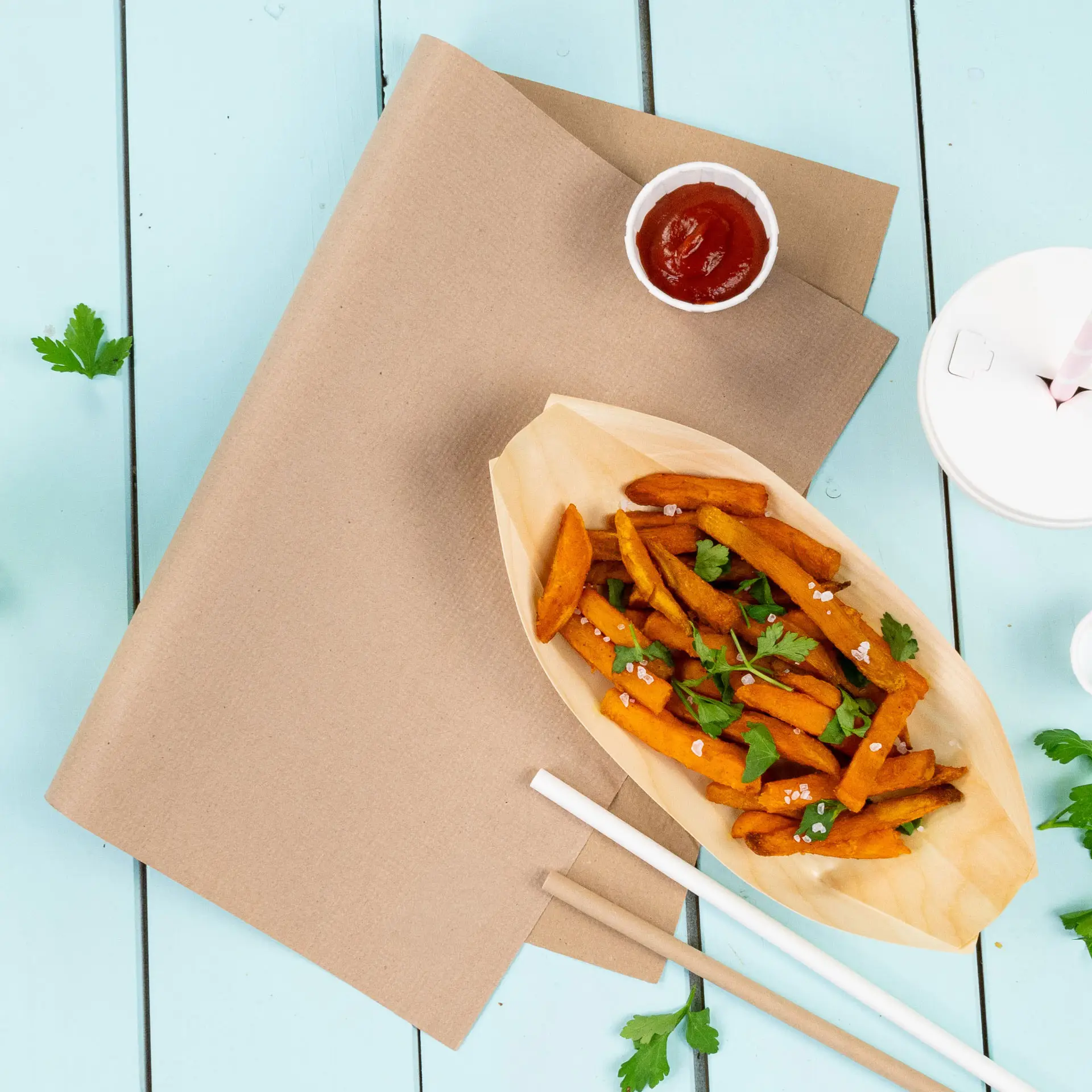 Bruine papieren placemat met zoete aardappelfrites in een bootvormige container, ketchup en koriander op een blauwe achtergrond.