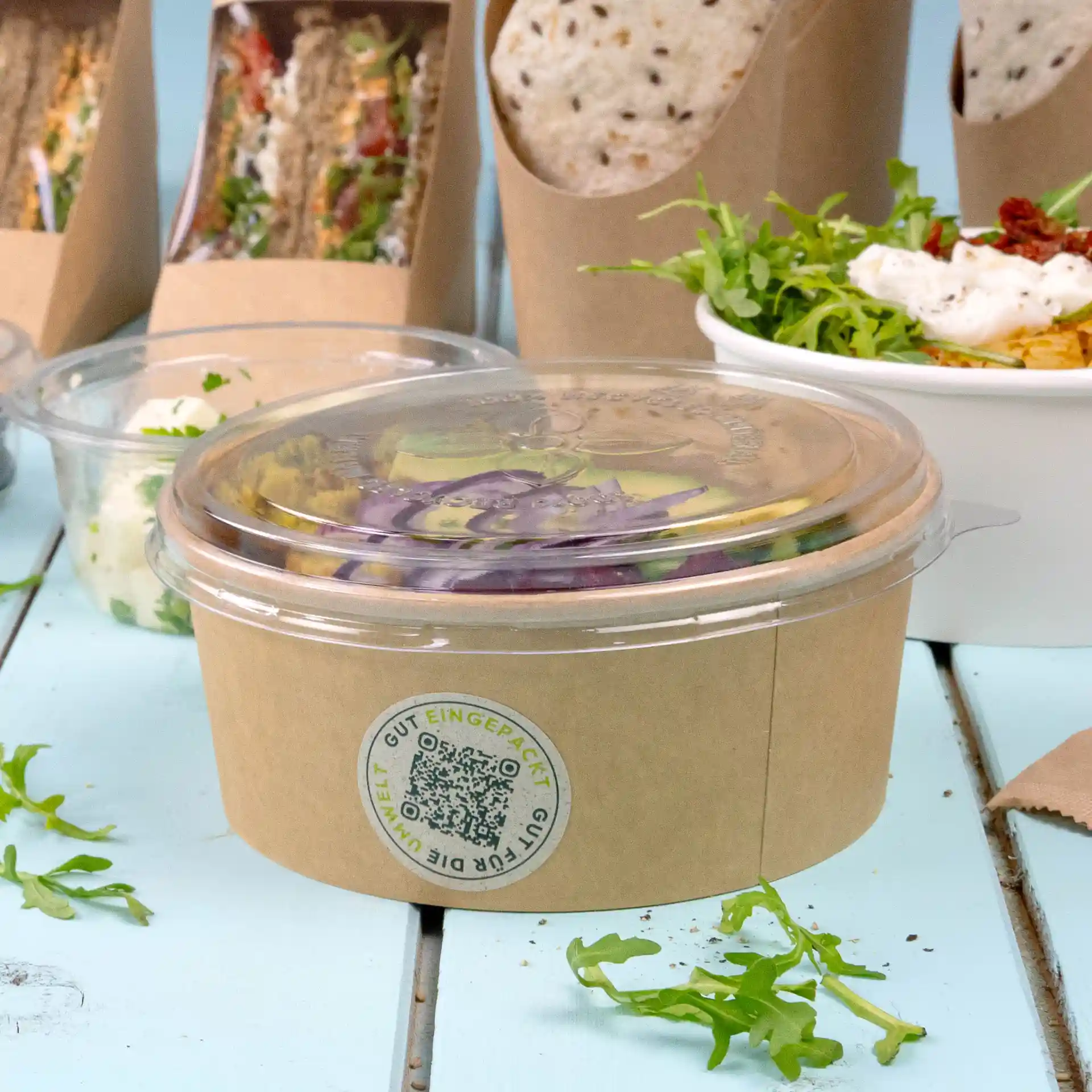 Transparante ronde beker met een deksel, gevuld met salade en een label met een cirkelontwerp.