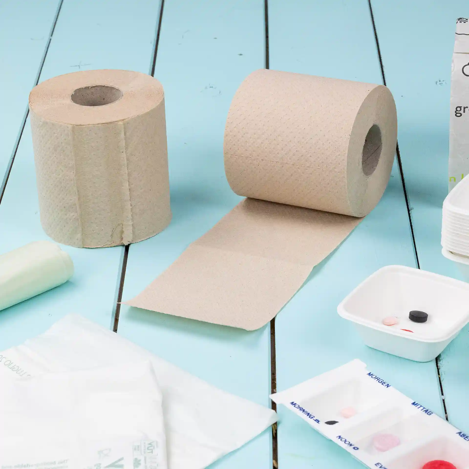 Twee rollen bruin toiletpapier van gerecycled papier, 2-laags, met één rol gedeeltelijk uitgerold op een blauwe ondergrond.