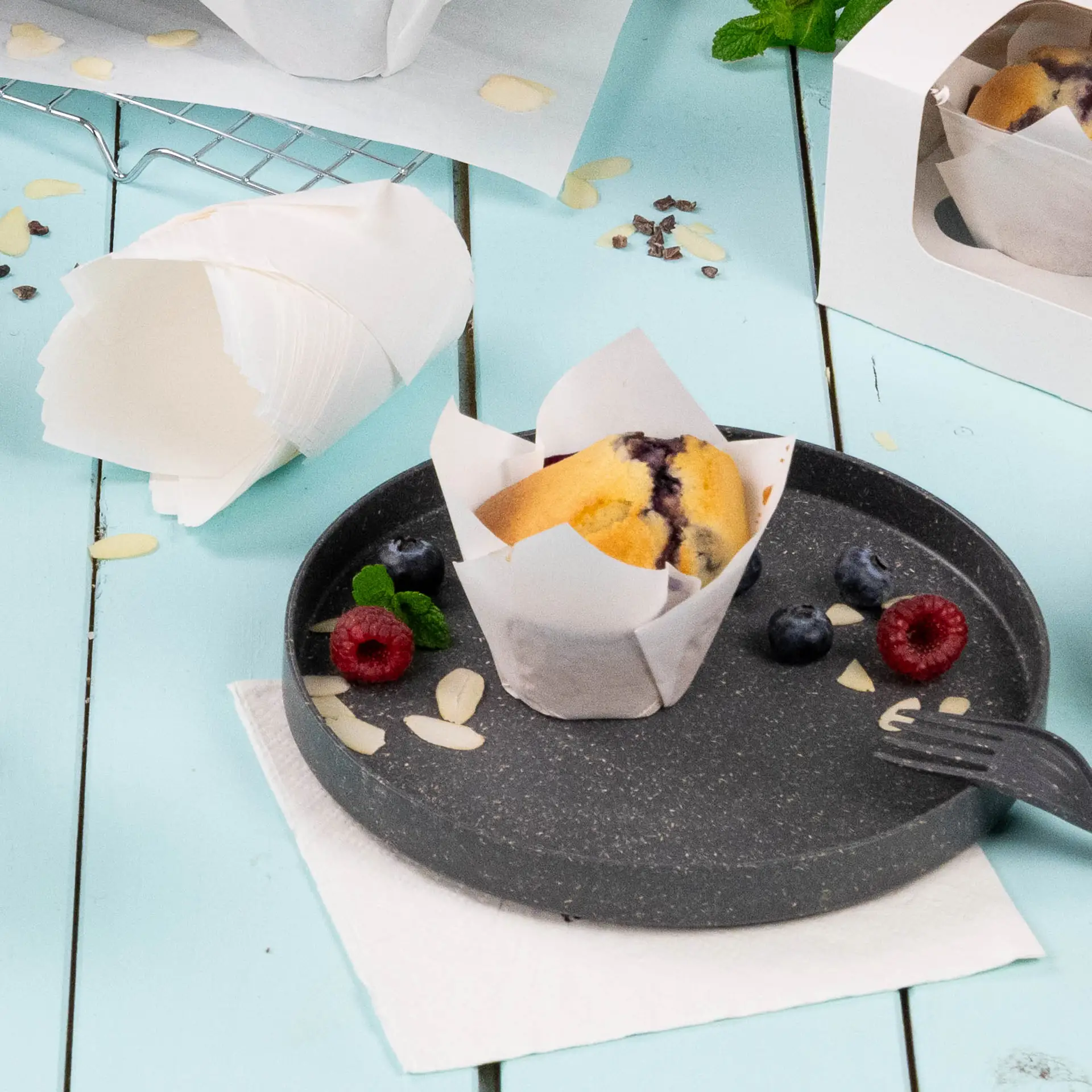 Een wit muffinbekertje met vetvrij papier op een donker bord; gegarneerd met frambozen, bosbessen en amandelschaafsel.