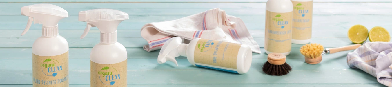 Twee sprayflessen met schoonmaakoplossing, een doek, een schrobborstel en gehalveerde limoenen op een blauwe houten ondergrond.