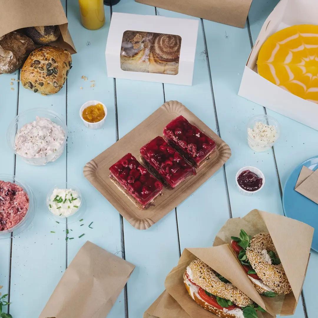 Diverse gebakken goederen en desserts op een blauwe tafel, waaronder jellytaarten, sandwiches en dips in containers.