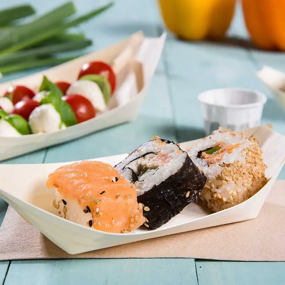 Sushirollen geserveerd in een houten bootvormig gerecht, met zalm, sesam en nori, met een bijgerecht van cherrytomaten en mozzarella.