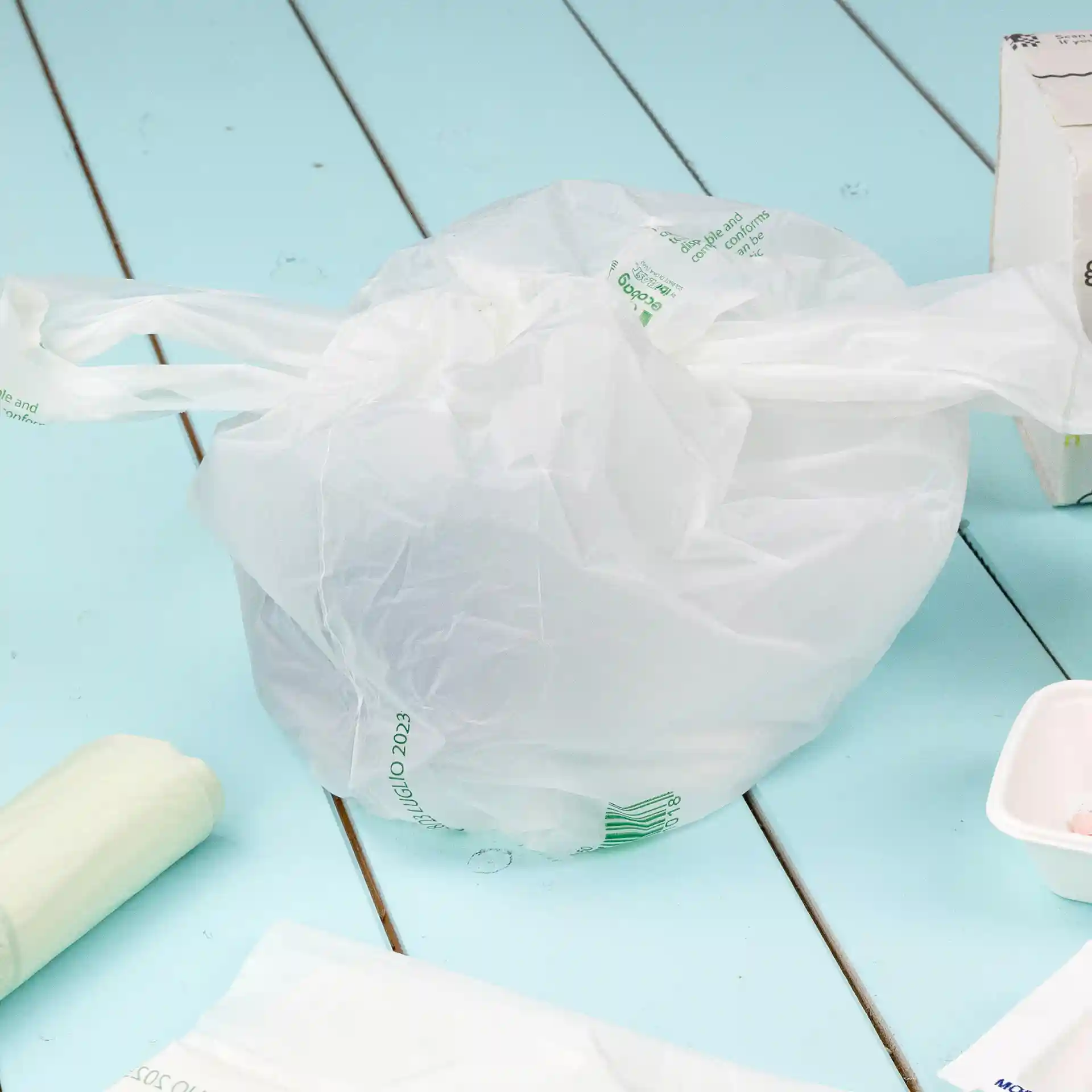Transparante tas van PLA-materiaal, bovenaan gestrikt, op een blauwe ondergrond geplaatst.