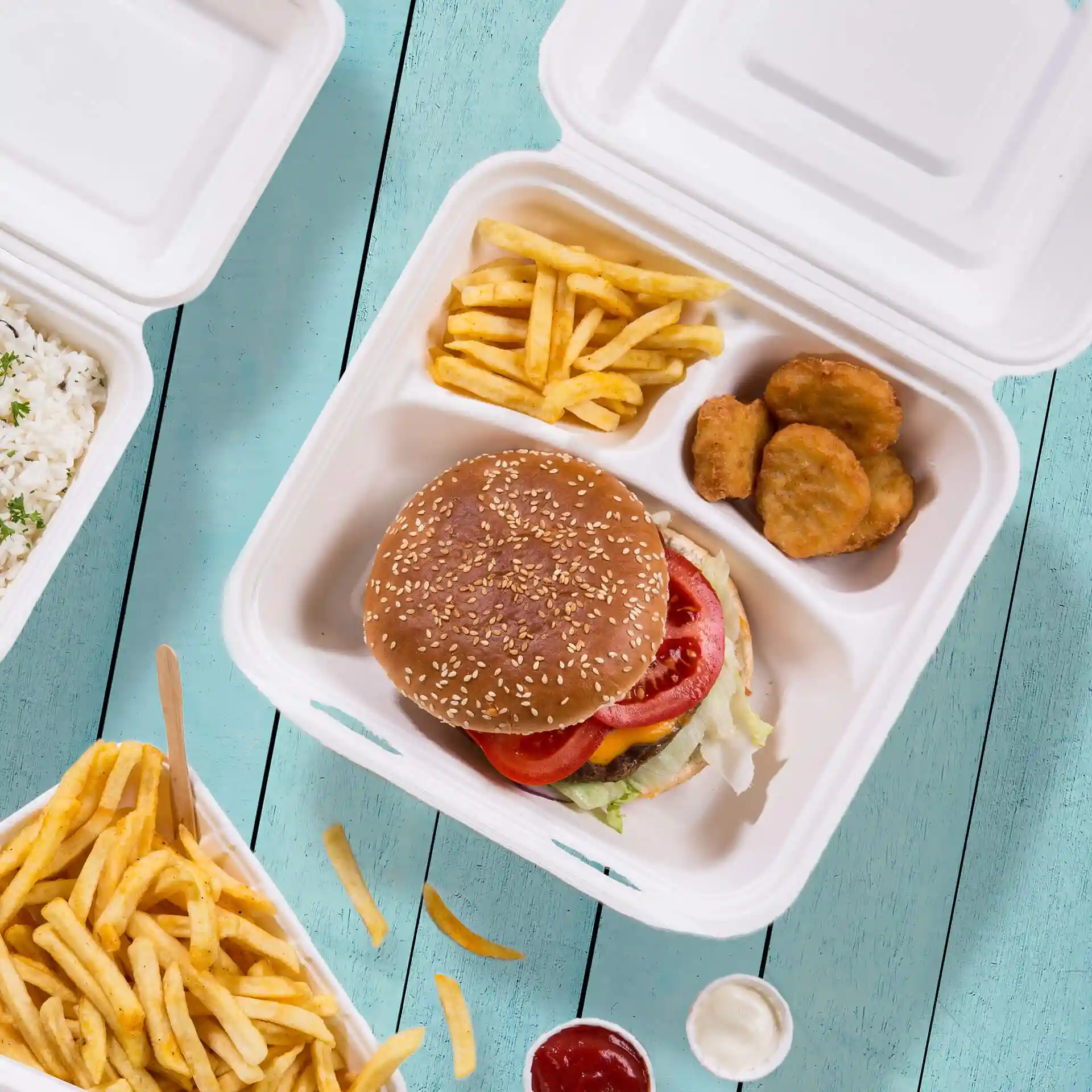 Afbeelding van een witte suikerrietcontainer met drie compartimenten, met een burger, friet en kipnuggets.