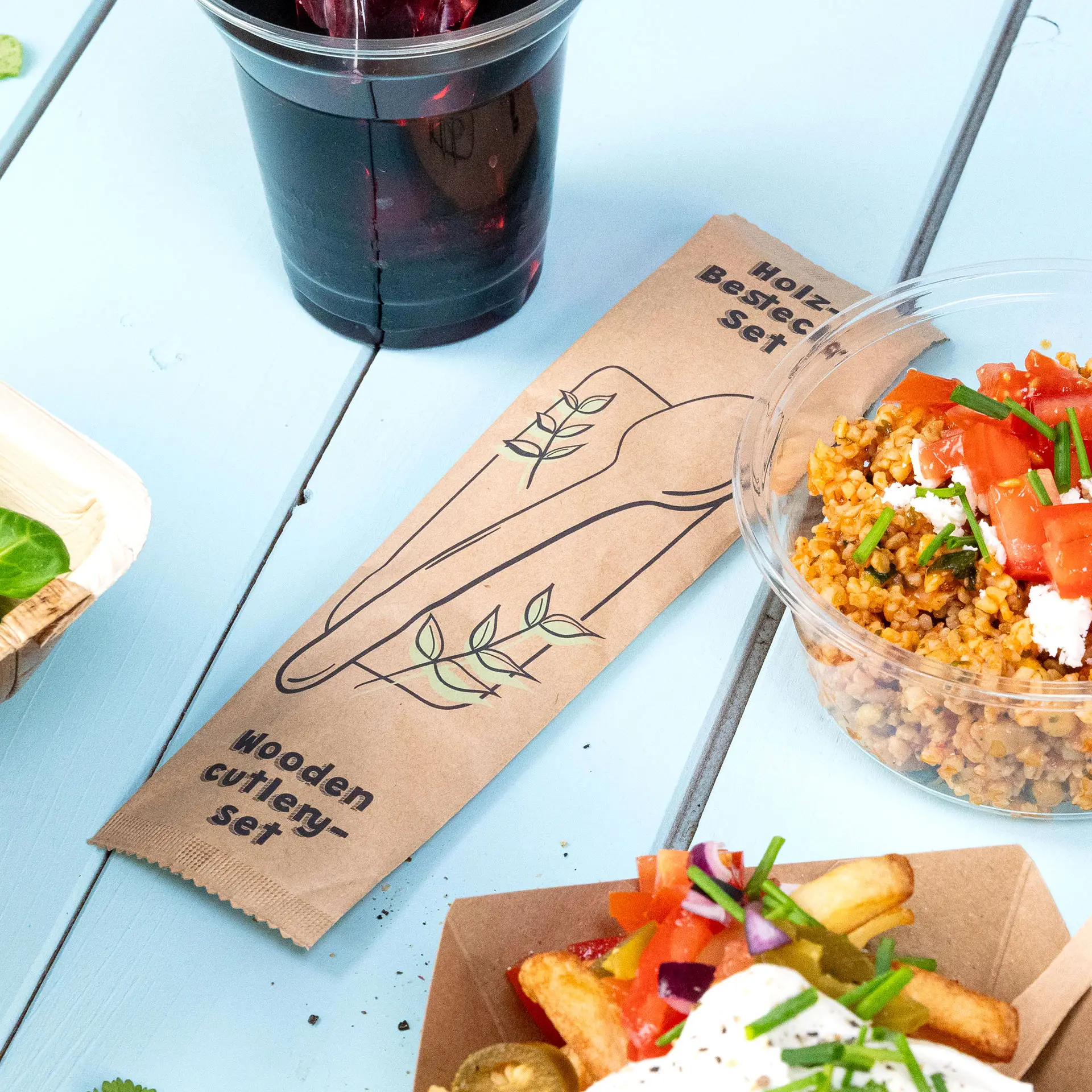 Houten bestekset met lepel en servet getoond; bevat een biologisch afbreekbare zak en is geschikt voor warme of koude voeding.