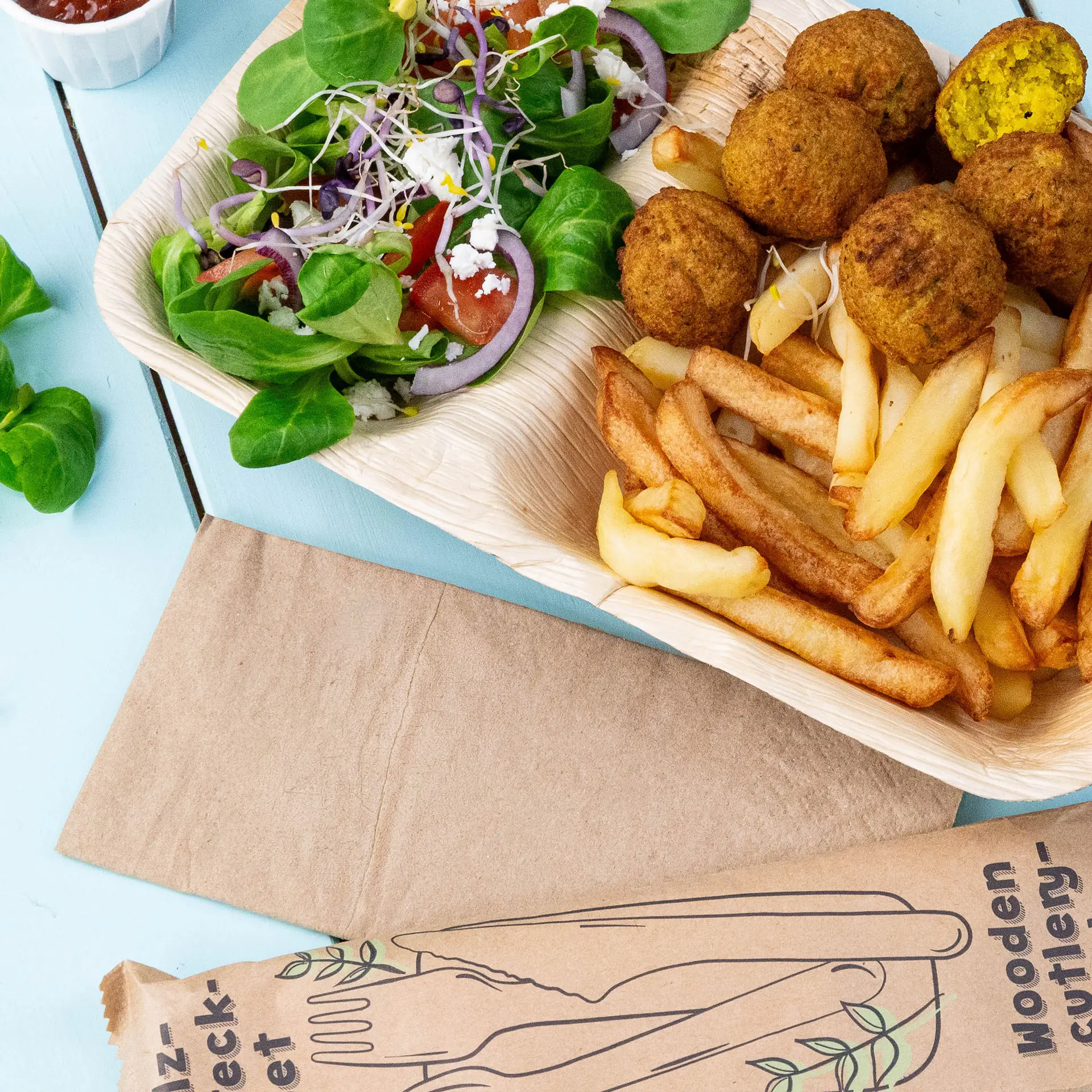 Afbeelding van een houten dienblad met falafelballetjes, friet en een gemengde salade met groen, tomaten en uien.