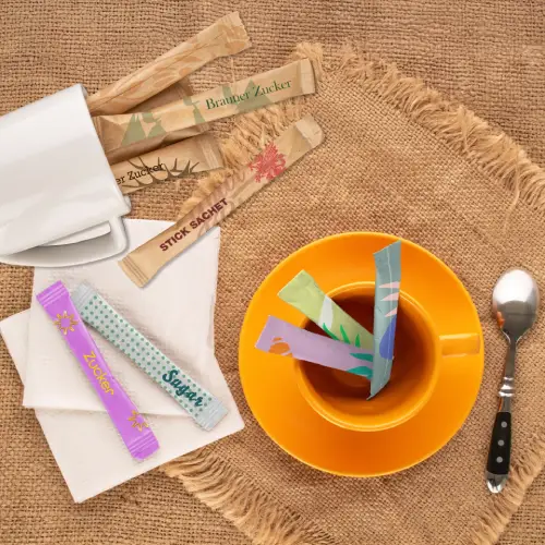 Kleurige suikerstokjes in een kop thee op een rustiek tafelblad met een lepel en lege bekers.
