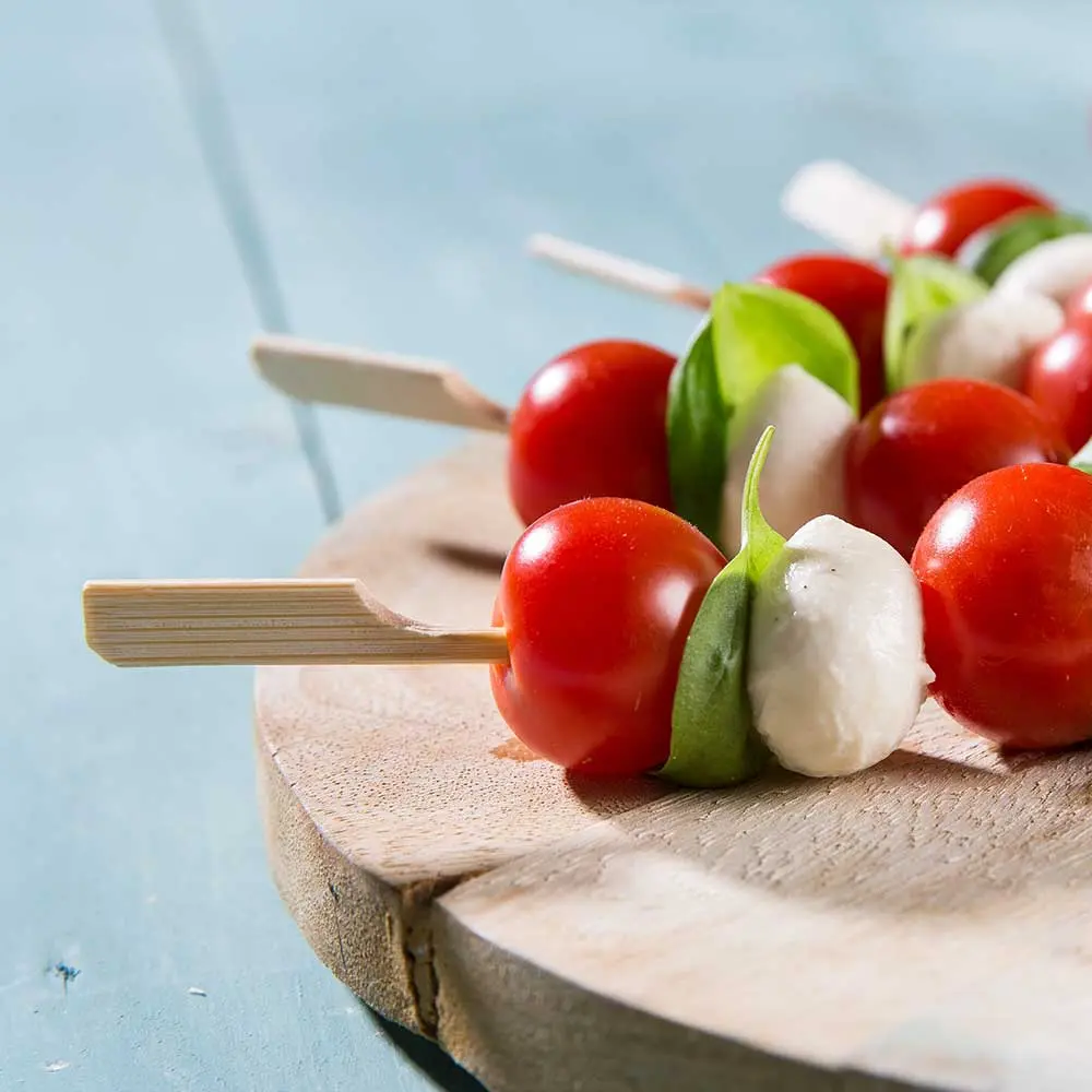 Spiesjes met cherrytomaten, basilic en mozzarella ballen op een houten plank.