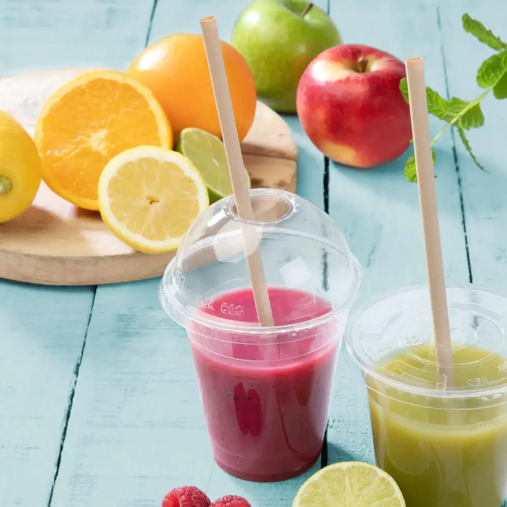 Twee transparante bekers met fruitsmoothies, één roze en één groen, naast verse vruchten op een blauwe ondergrond.