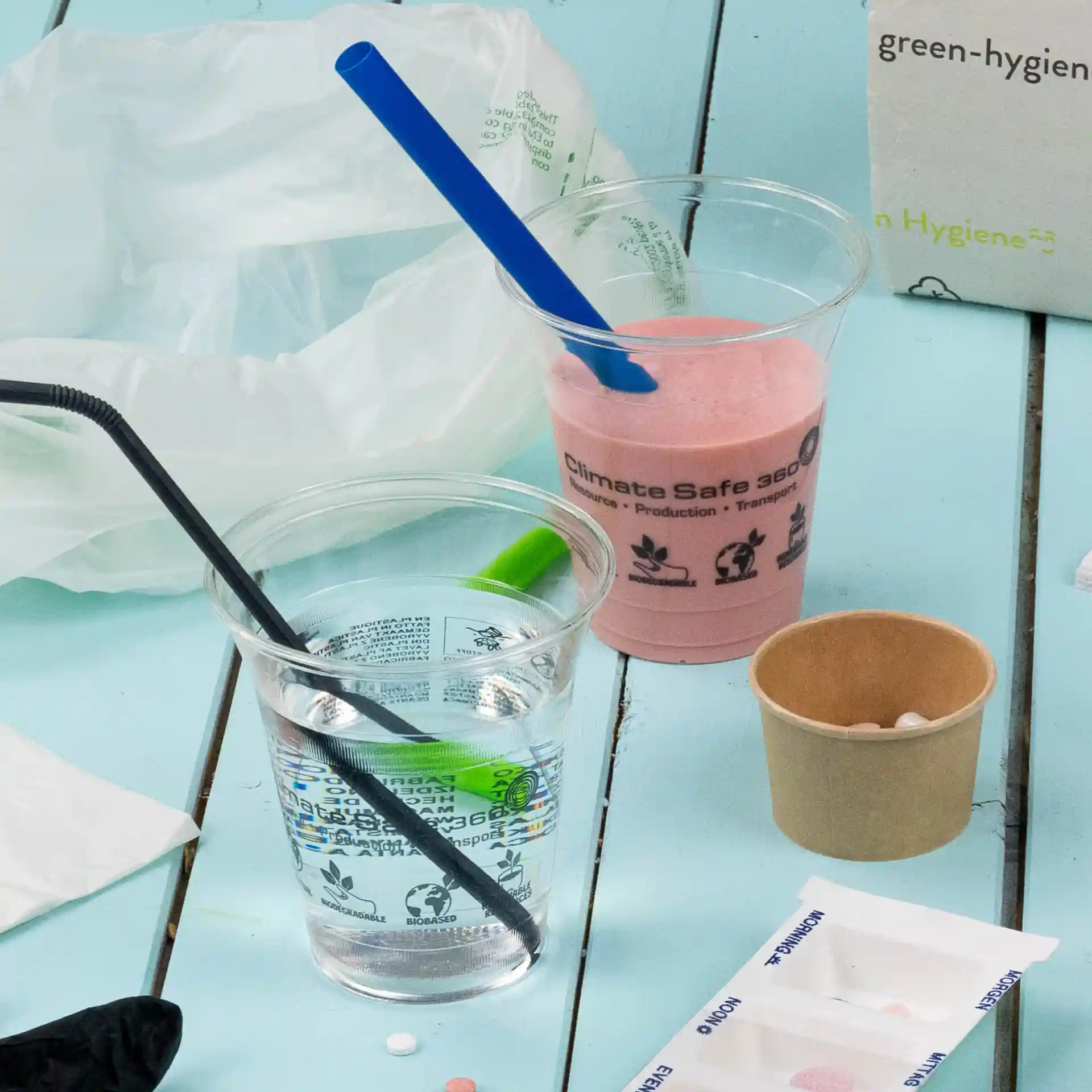 Transparante beker met een blauwe rietje met roze smoothie, naast een heldere beker met water en een zwart rietje.