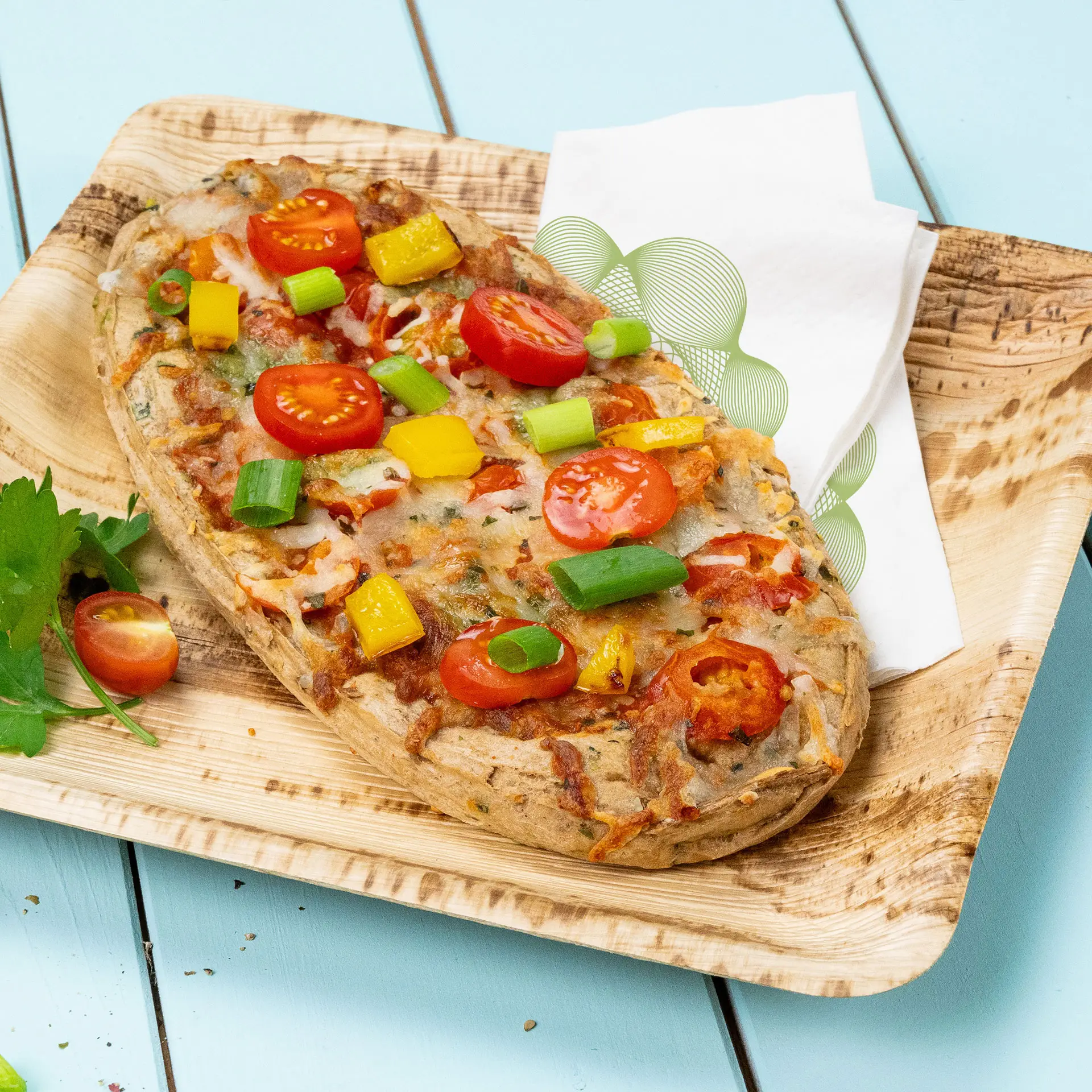 Groentepizza belegd met cherrytomaten, lente-uitjes en gele paprika op een houten bord met een servet.