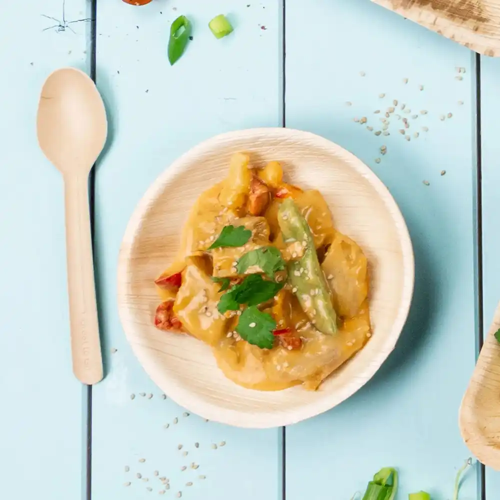 Bamboekom met roergebakken groenten en saus, getopt met sesamzaad en koriander, naast een houten lepel.