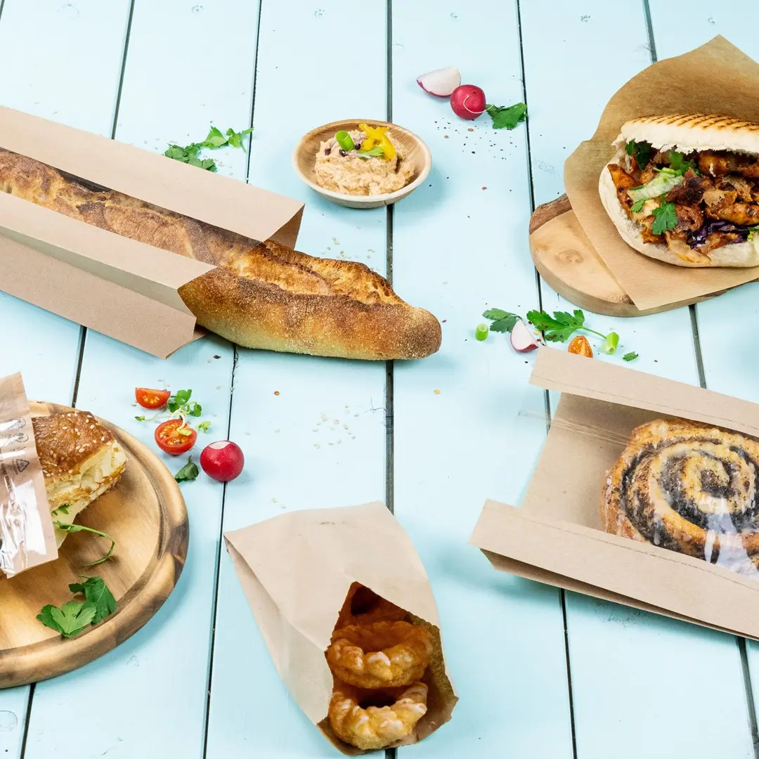 Afbeelding van verschillende gebakken goederen, waaronder een baguette, sandwich, gebak en een kom dip op een blauwe houten ondergrond.