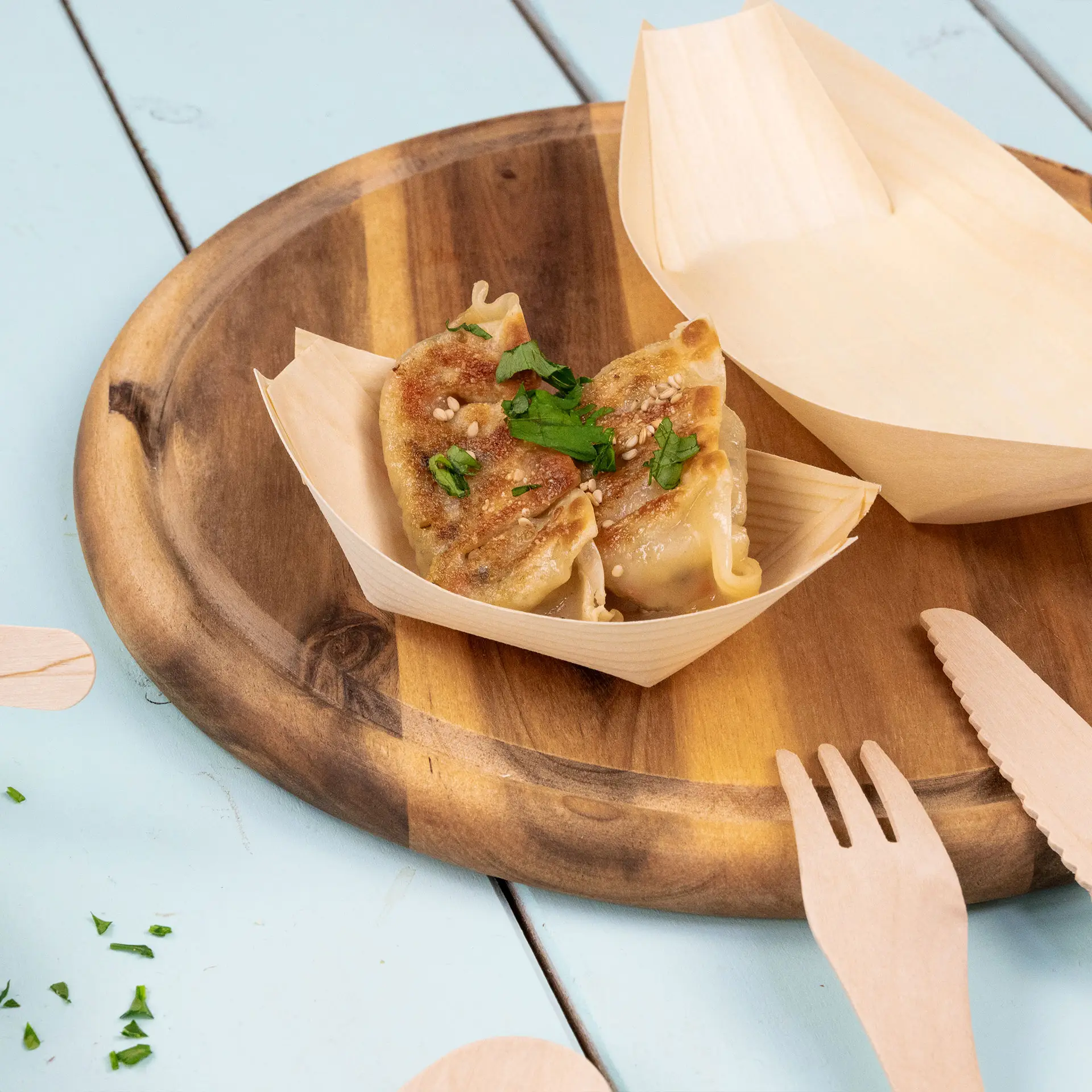 Houten bootvormige container met twee dumplings, getopt met sesamzaad en peterselie op een houten schaal.