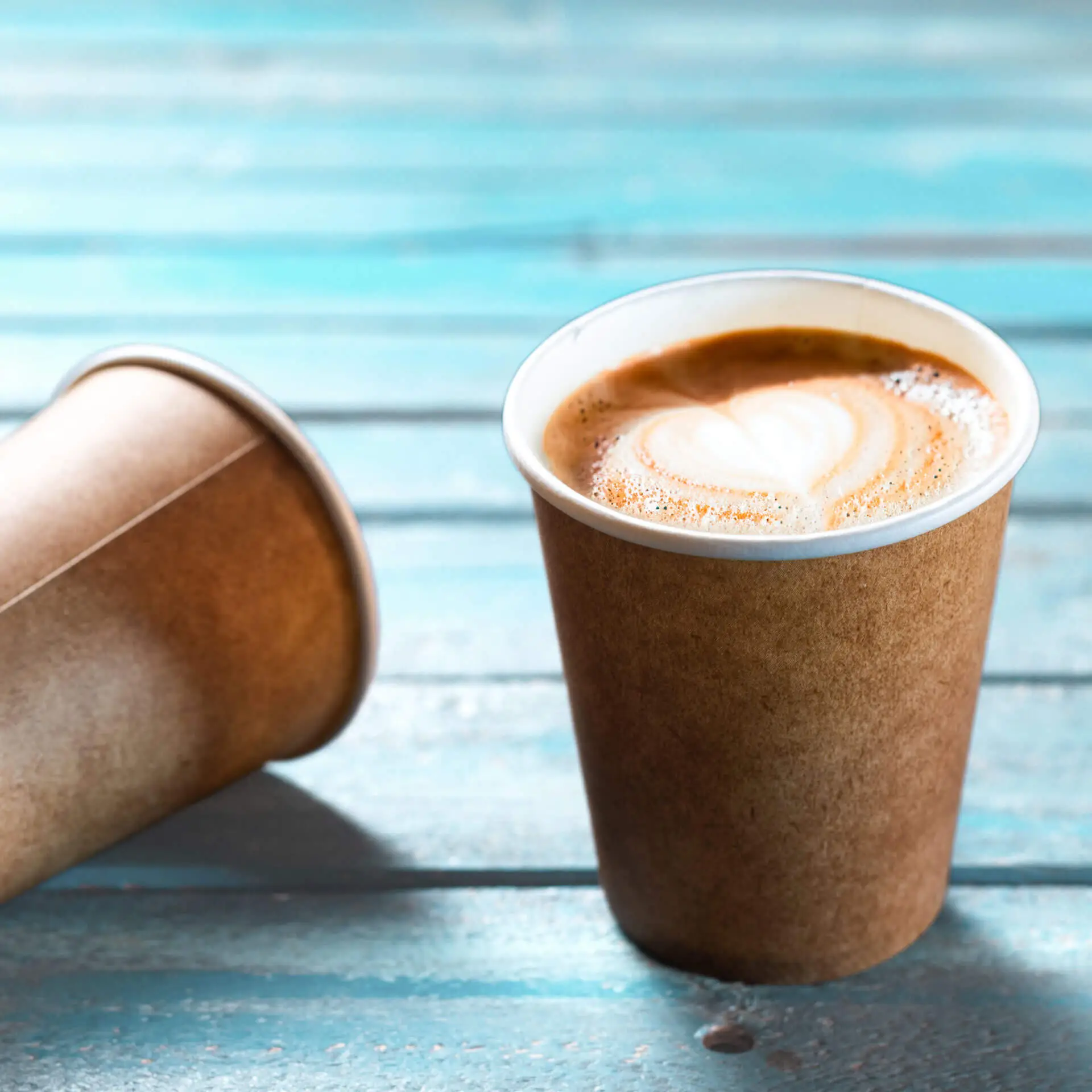 Bruine papieren beker met een witte binnenvoering, gevuld met koffie, op een blauwe houten ondergrond.