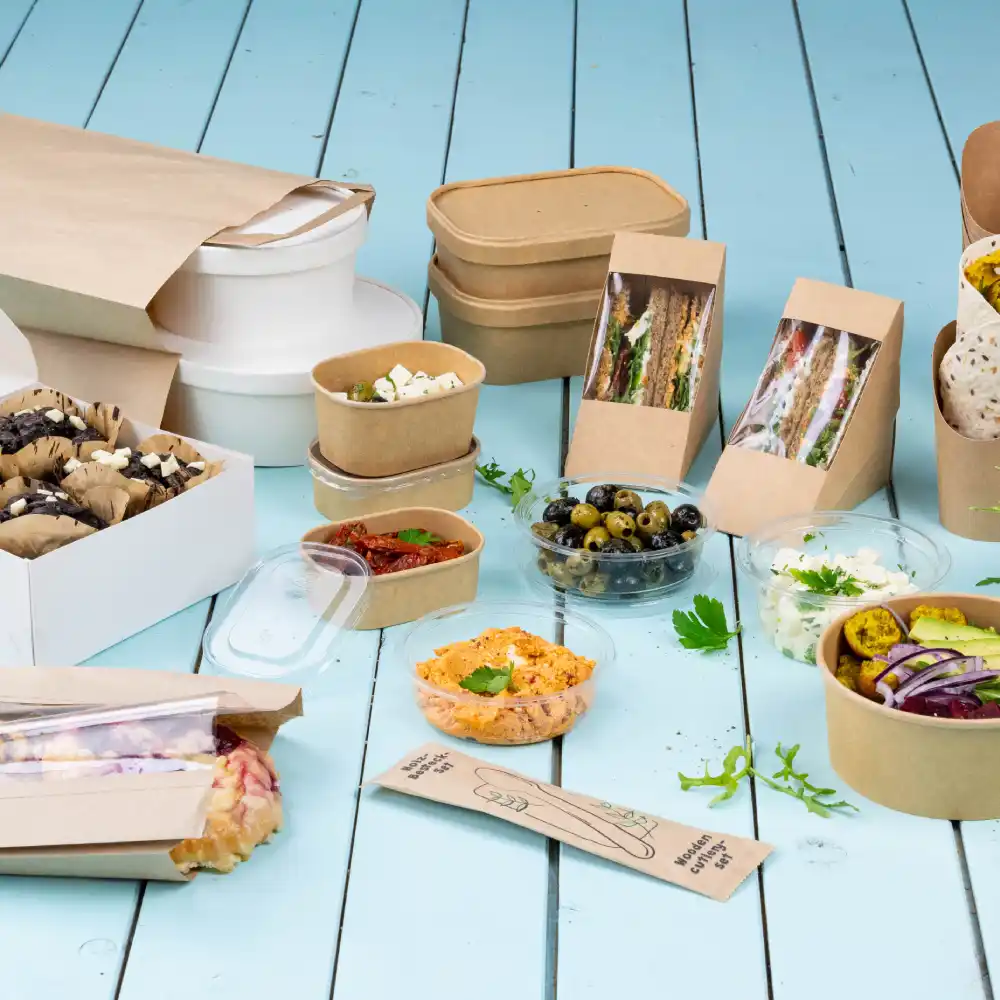 Een assortiment voedselcontainers omvat papieren dozen, kommen en doorzichtige plastic bekers met verschillende gerechten en snacks.