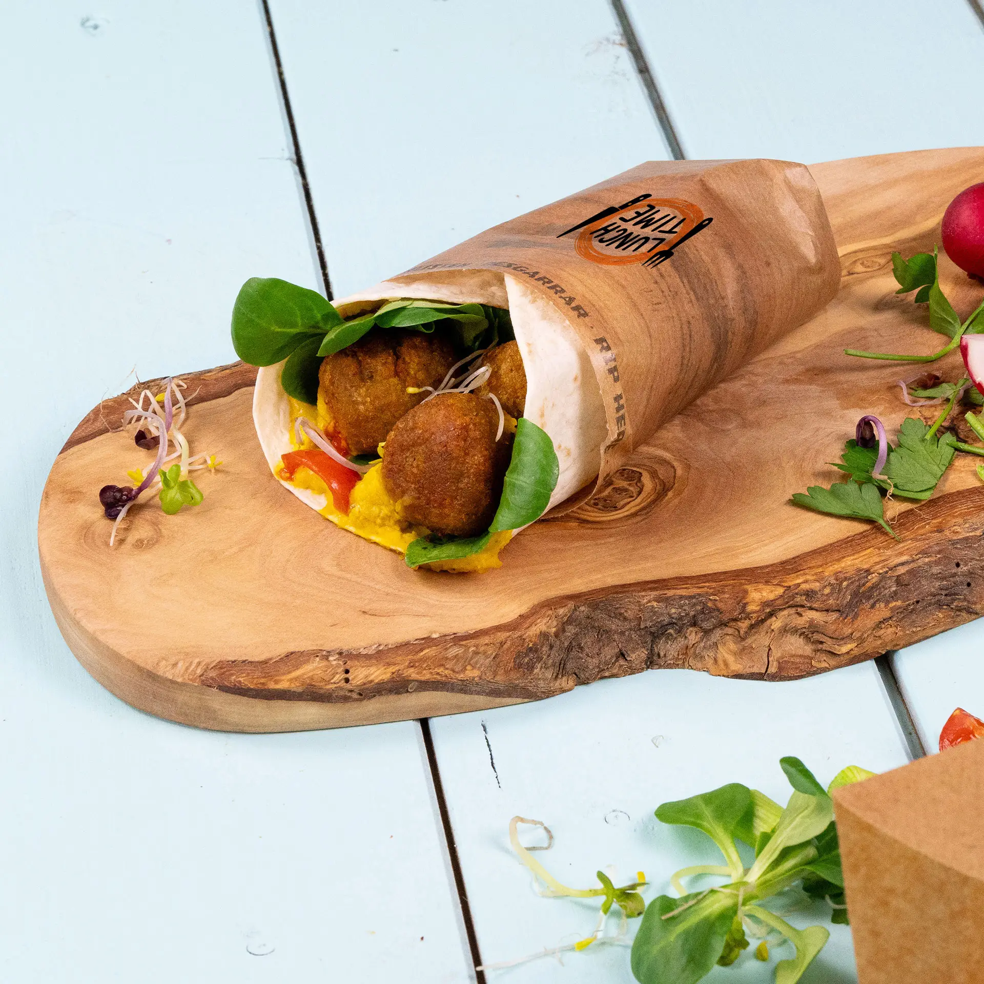 Een op maat gedrukt wikkelzakje met falafel, groenten en saus, geplaatst op een houten serveerplank.