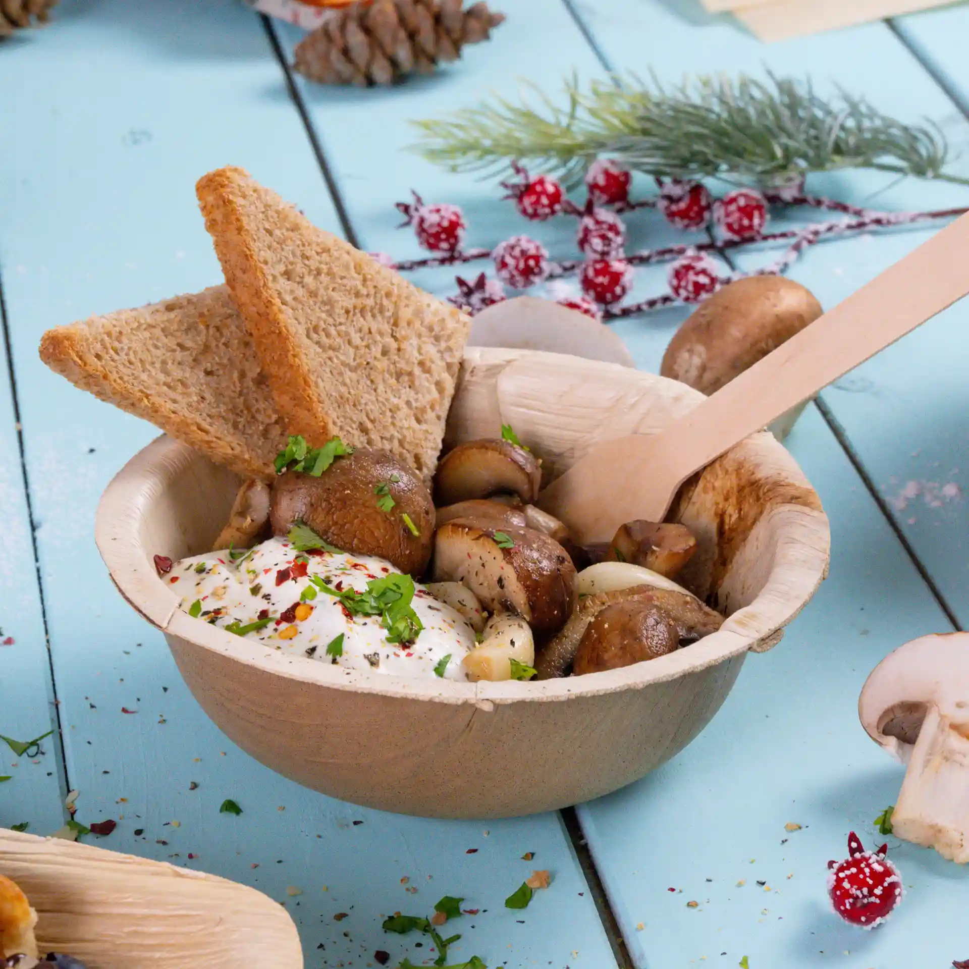 Kom van palmblad met champignons, een lepel saus en twee plakken bruin brood, met een houten lepel.