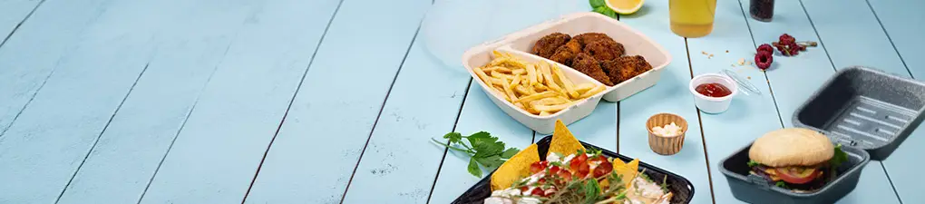 Chef-personage met een groene kop en een witte hoed, met een lepel; twee voedselcontainers met een burger en een maaltijd met friet en kip op een blauwe houten achtergrond.