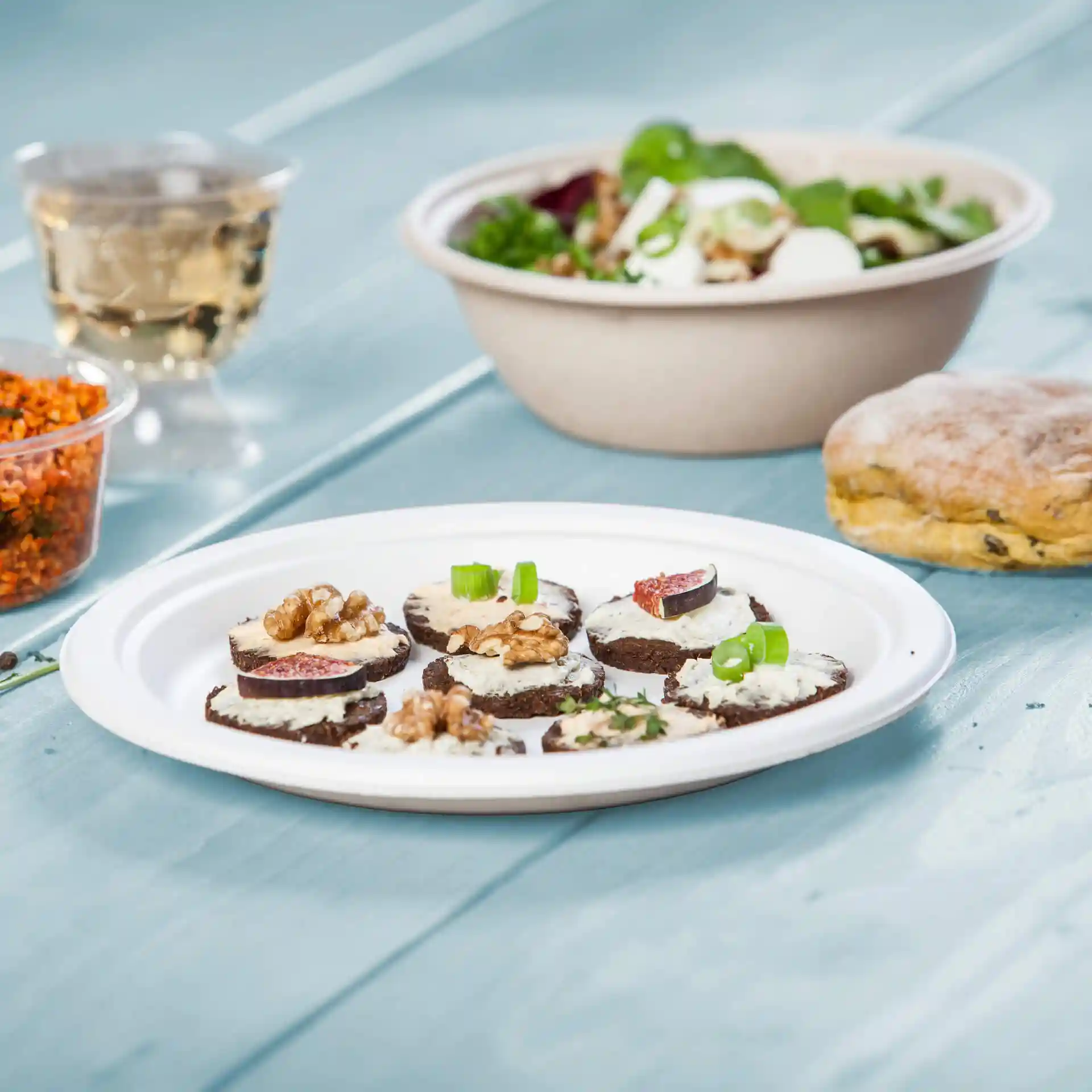 Bord met verschillende ronde plakken donker brood belegd met room, walnoten en vijgen, naast een salade en een koekje.