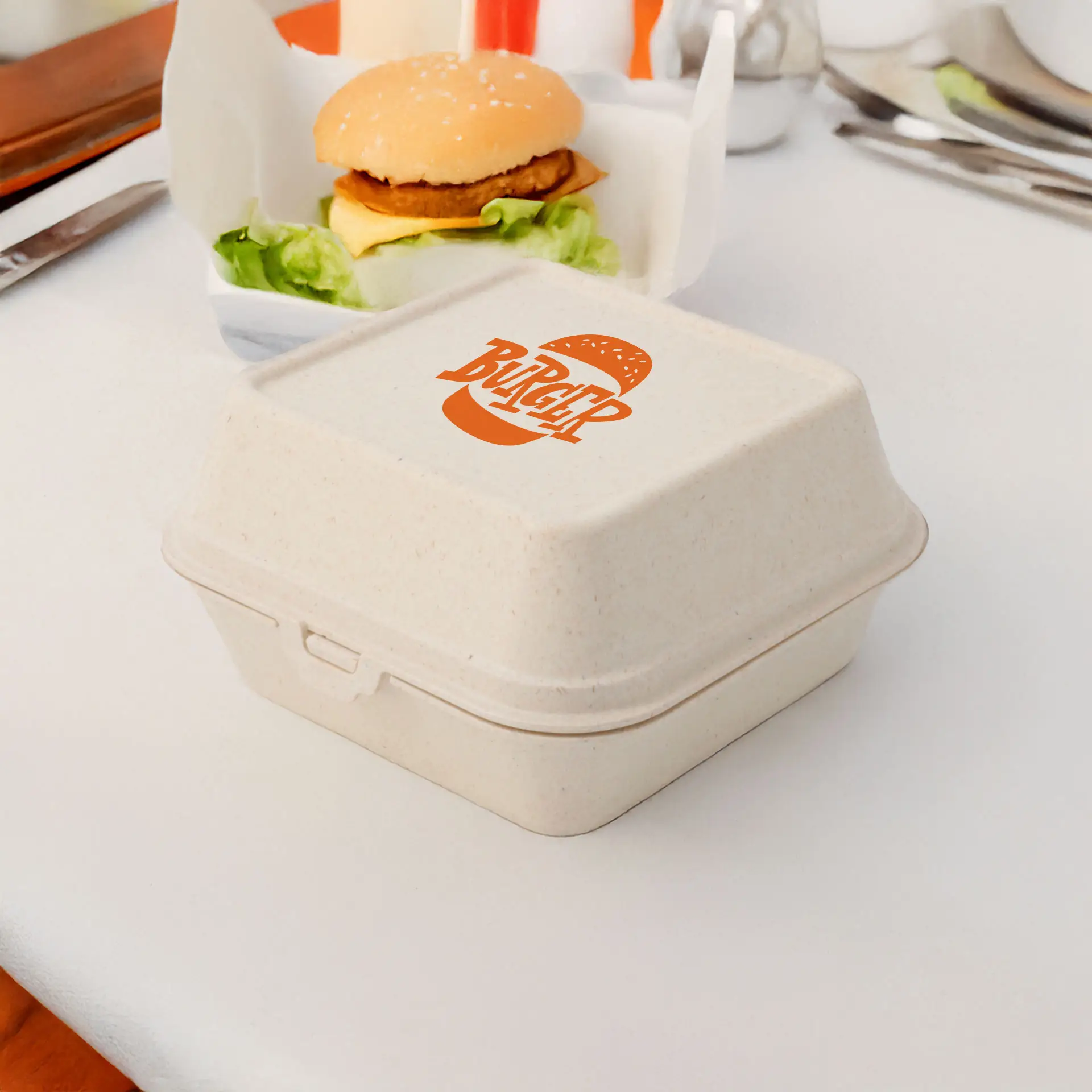 Crèmewitte herbruikbare burgerdoos met een bedrukt logo, geschikt voor warme en koude voedingsmiddelen, naast een burger op een tafel.