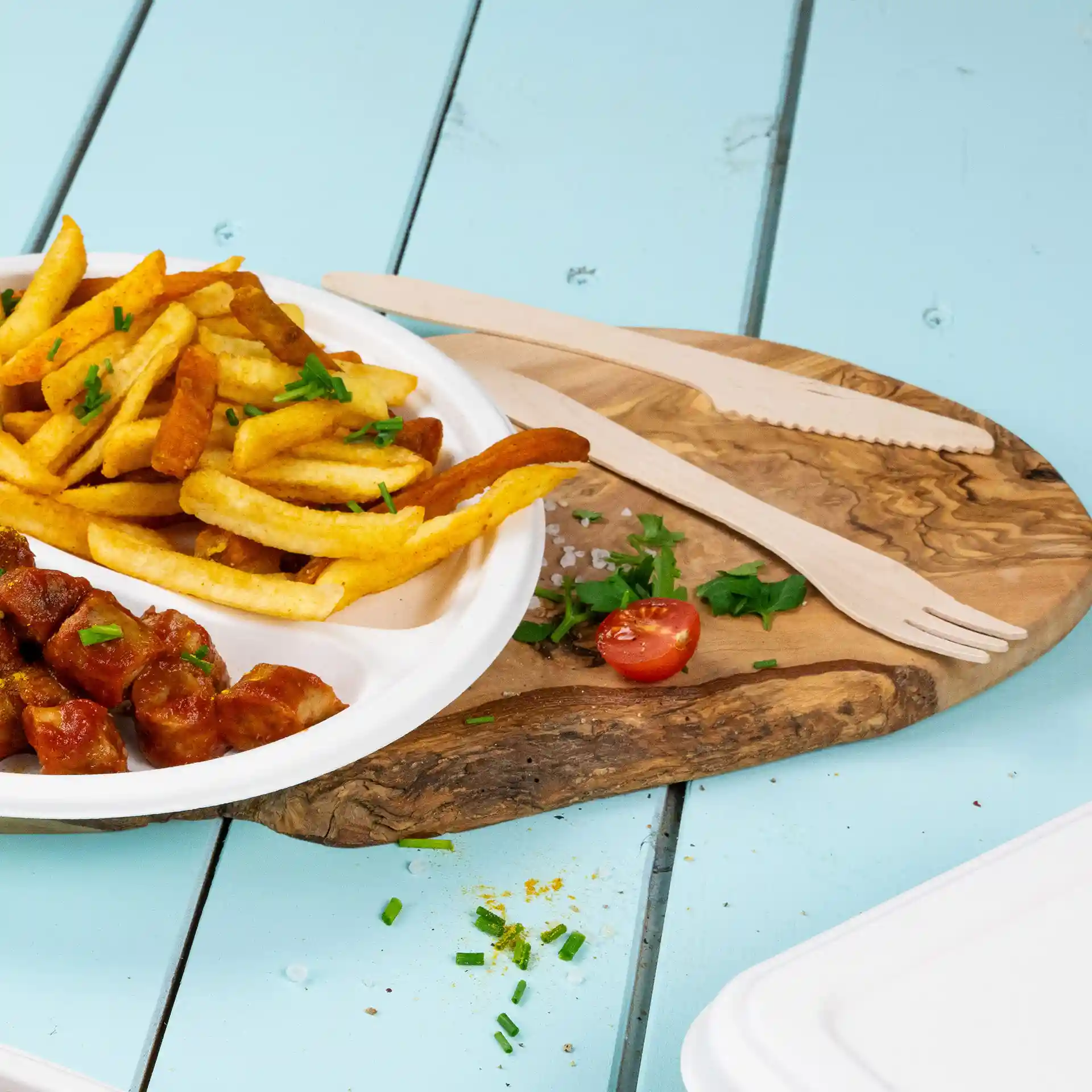 Afbeelding van een bord met friet en worst, vergezeld van houten bestek op een houten serveerplank.
