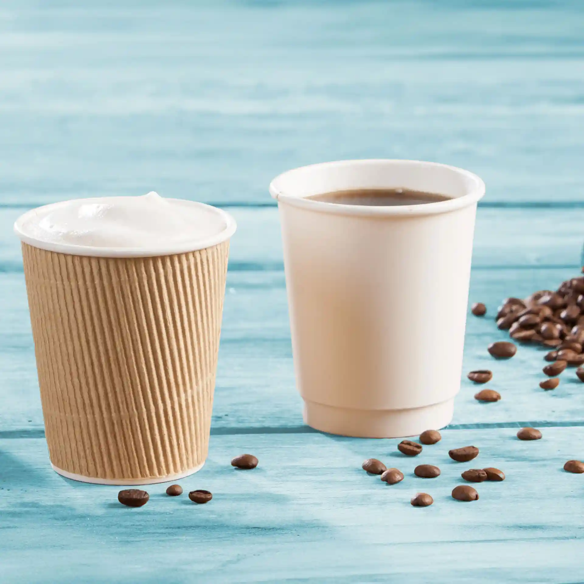 Dubbelwandige kartonnen bekers in bruin en wit, met koffiebonen verspreid over een blauwe houten ondergrond.