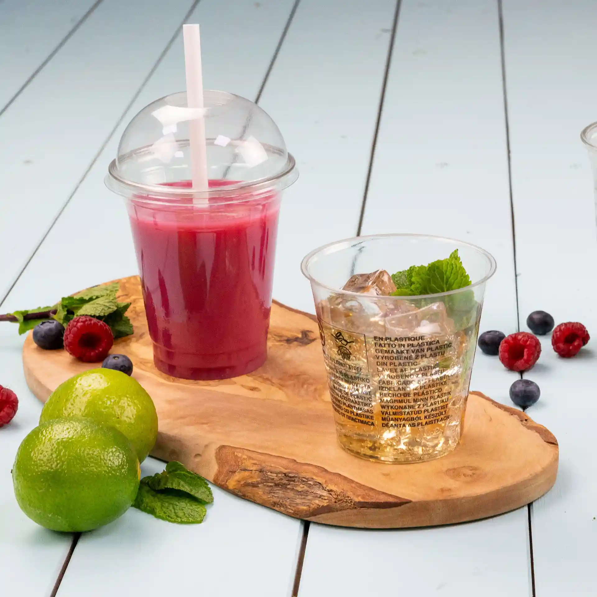 Transparante 12 oz rPET beker met ijs en munt, naast een roze drankje in een beker met een dome deksel, op een houten plank.