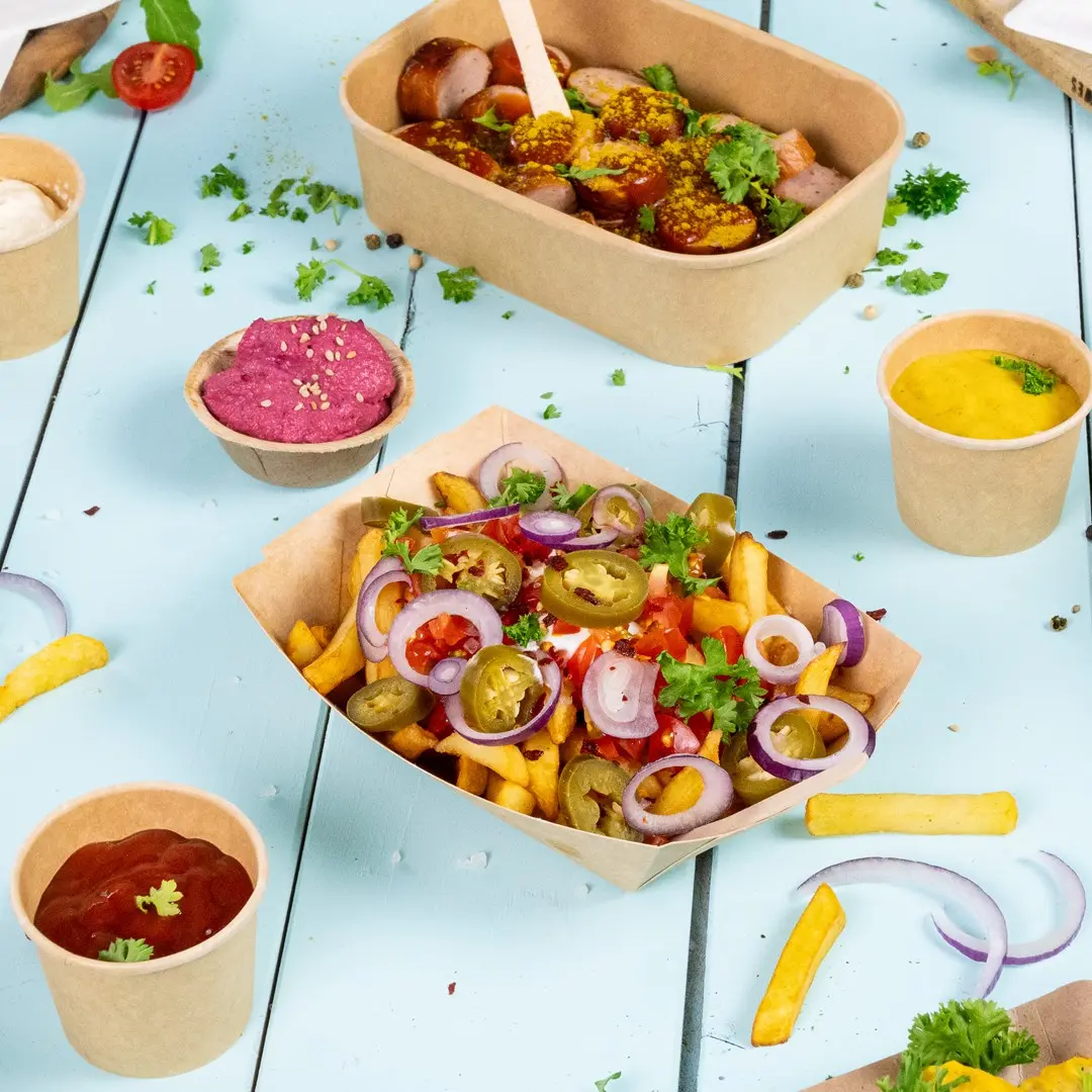 Afbeelding van verschillende voedingsmiddelen, waaronder een container met worstjes, een doos met loaded fries en kleine bekers met sauzen op een blauwe houten ondergrond.