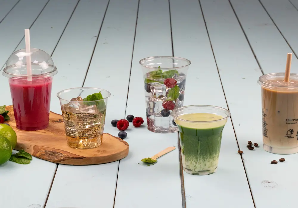 Vijf bekers met verschillende dranken op een houten dienblad, met roze, groene, heldere en bruine dranken met fruit en munt.