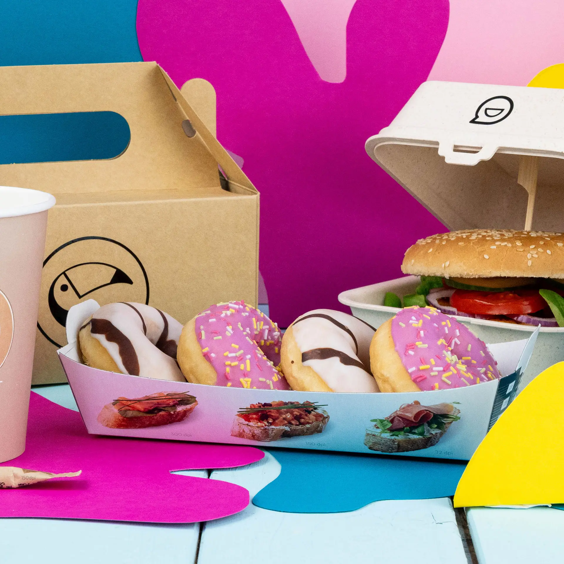 Rechthoekige witte snacktray met vier donuts, een burger in een container en een roze beker op een kleurrijke achtergrond.