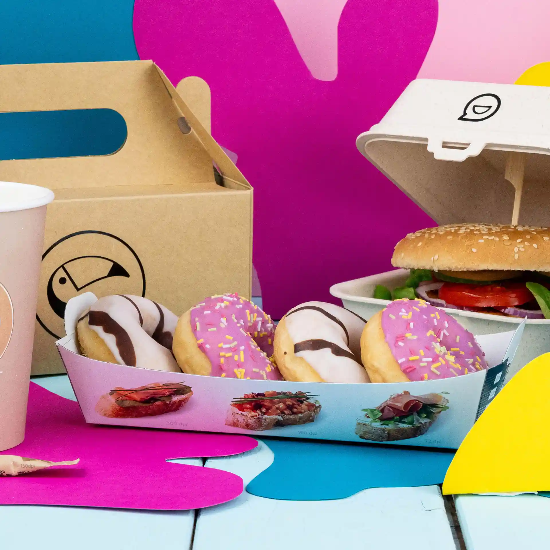 Rechthoekige witte snacktray met vier donuts, een burger in een container en een roze beker op een kleurrijke achtergrond.